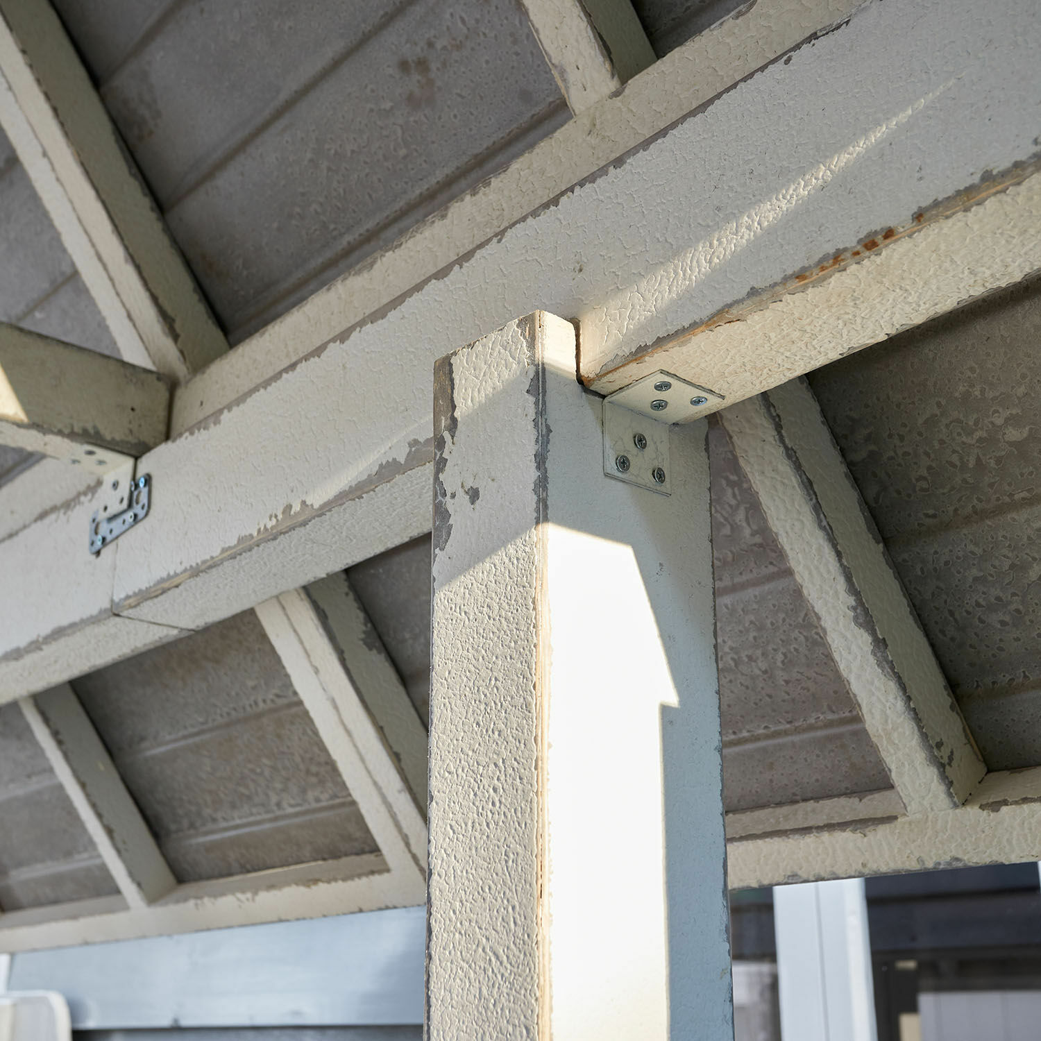 Weißer Metallpfosten und Träger mit abblätternder Farbe und sichtbaren Schrauben im Freien