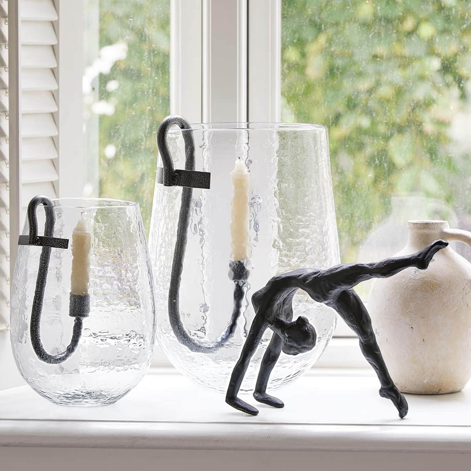 Glas-Kerzenhalter mit schwarzen Metallgriffen und weißen Kerzen, schwarze Tänzer-Skulptur auf Fensterbank