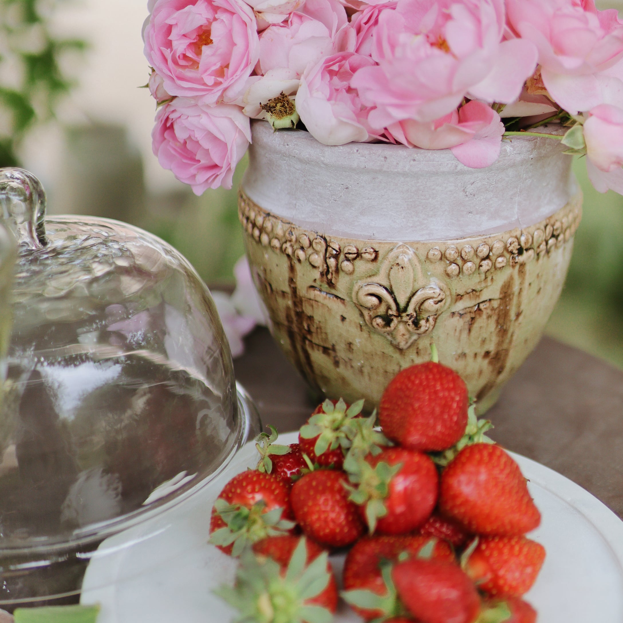 Keramiktopf mit rosa Blumen und frischen Erdbeeren auf weißem Teller