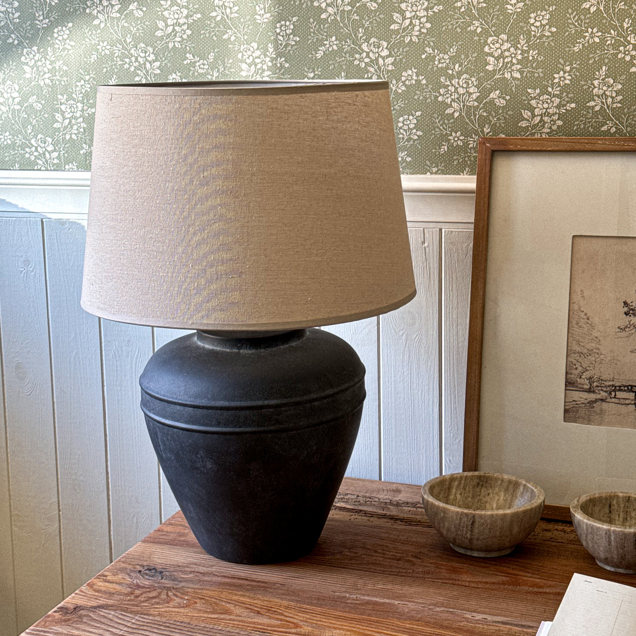 Tischlampe mit schwarzer Keramikbasis und beigem Lampenschirm auf Holztisch