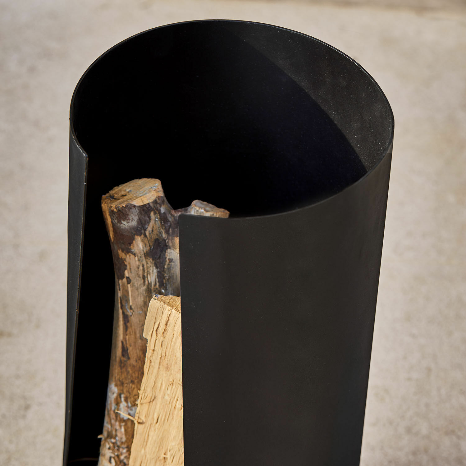 Schwarzer Metallbehälter für Brennholz mit naturbelassenen Holzscheiten, praktisch und robust