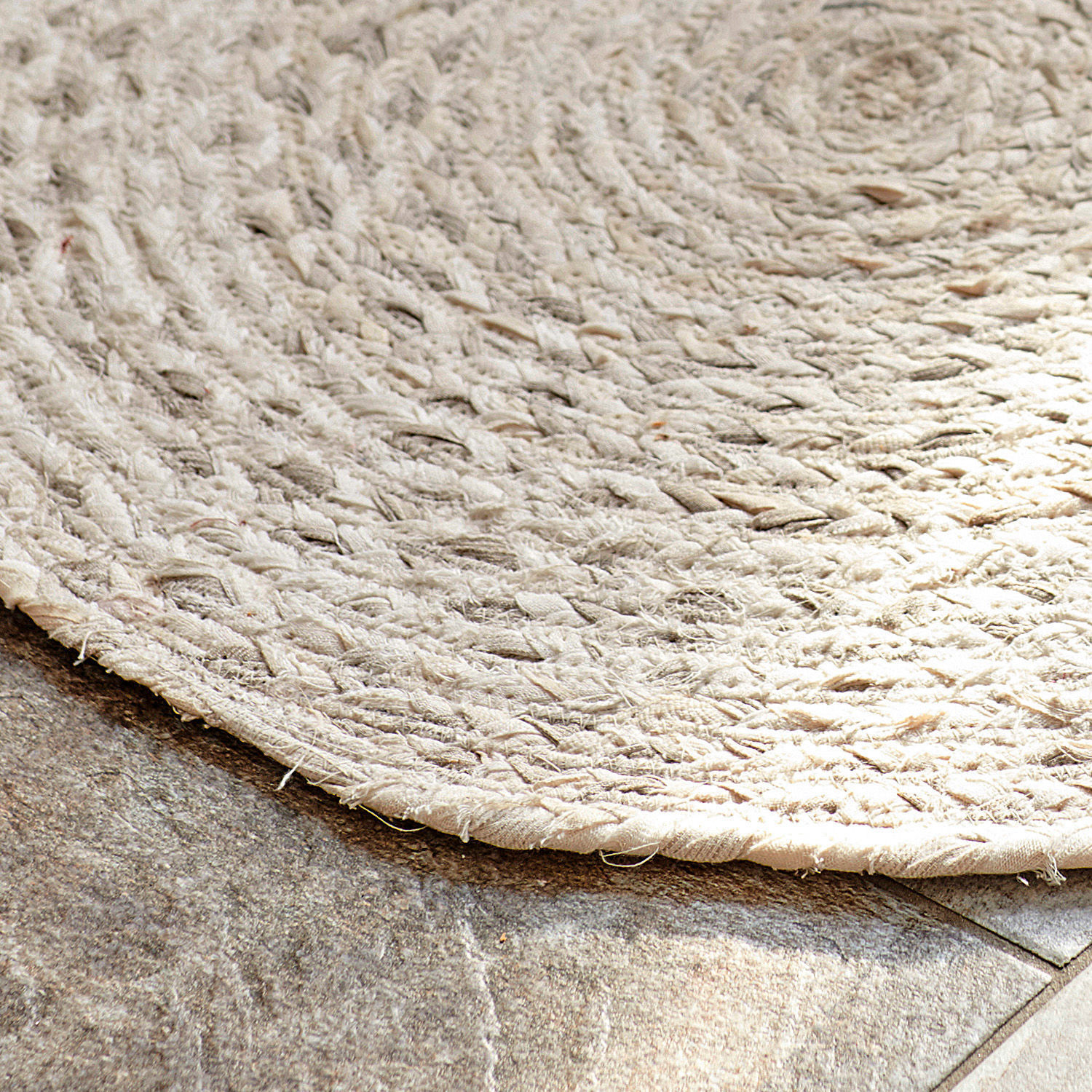 Runder Teppich aus geflochtenem Naturmaterial in hellem Beige auf Steinboden