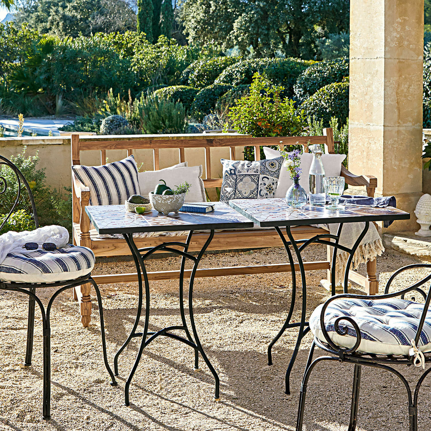 Garten mit Metallstühlen und Mosaiktischen, Holzbank mit Kissen, sommerliche Sitzgruppe