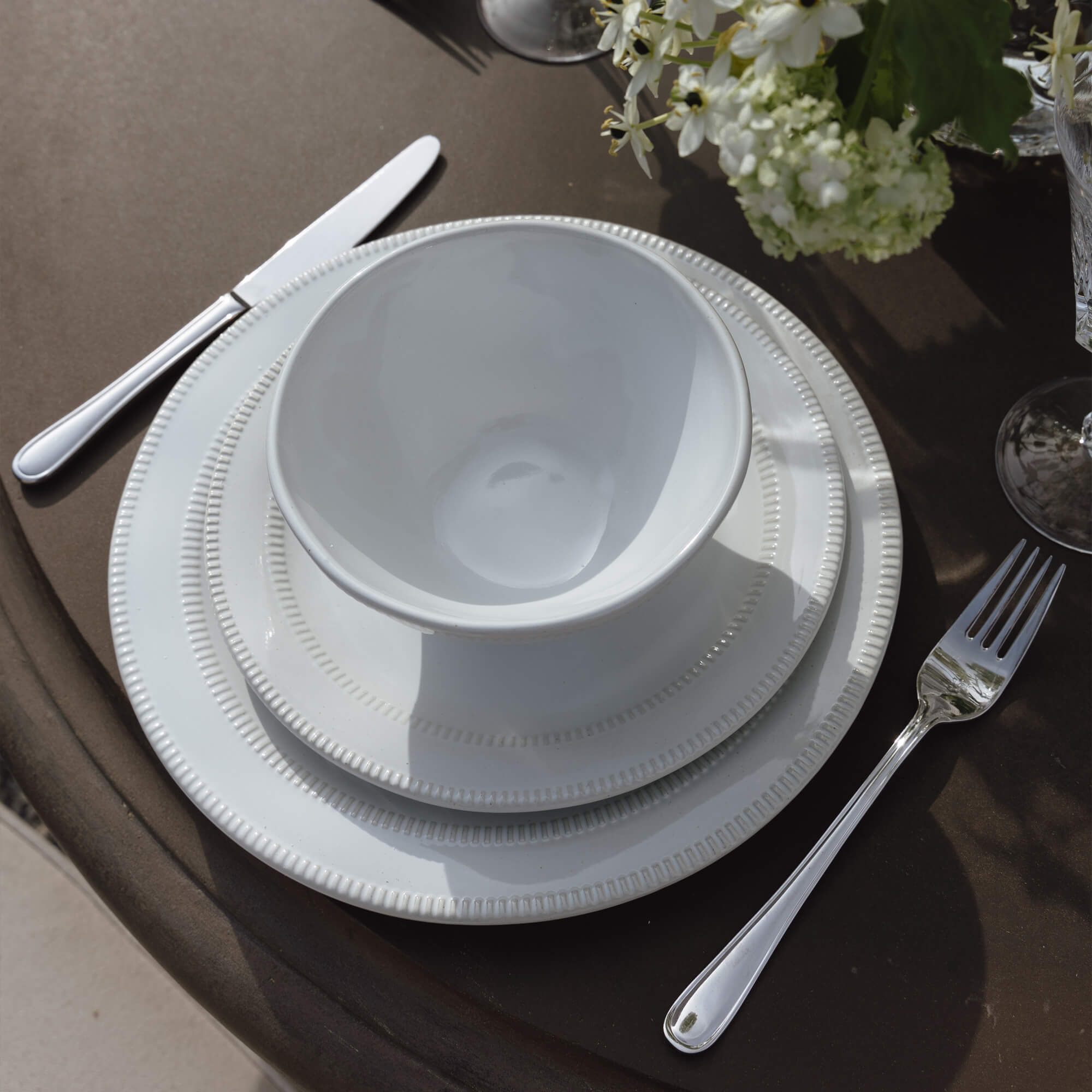 Weißes Porzellan-Geschirrset mit Schüssel und Tellern auf braunem Tisch mit Blumen und Besteck