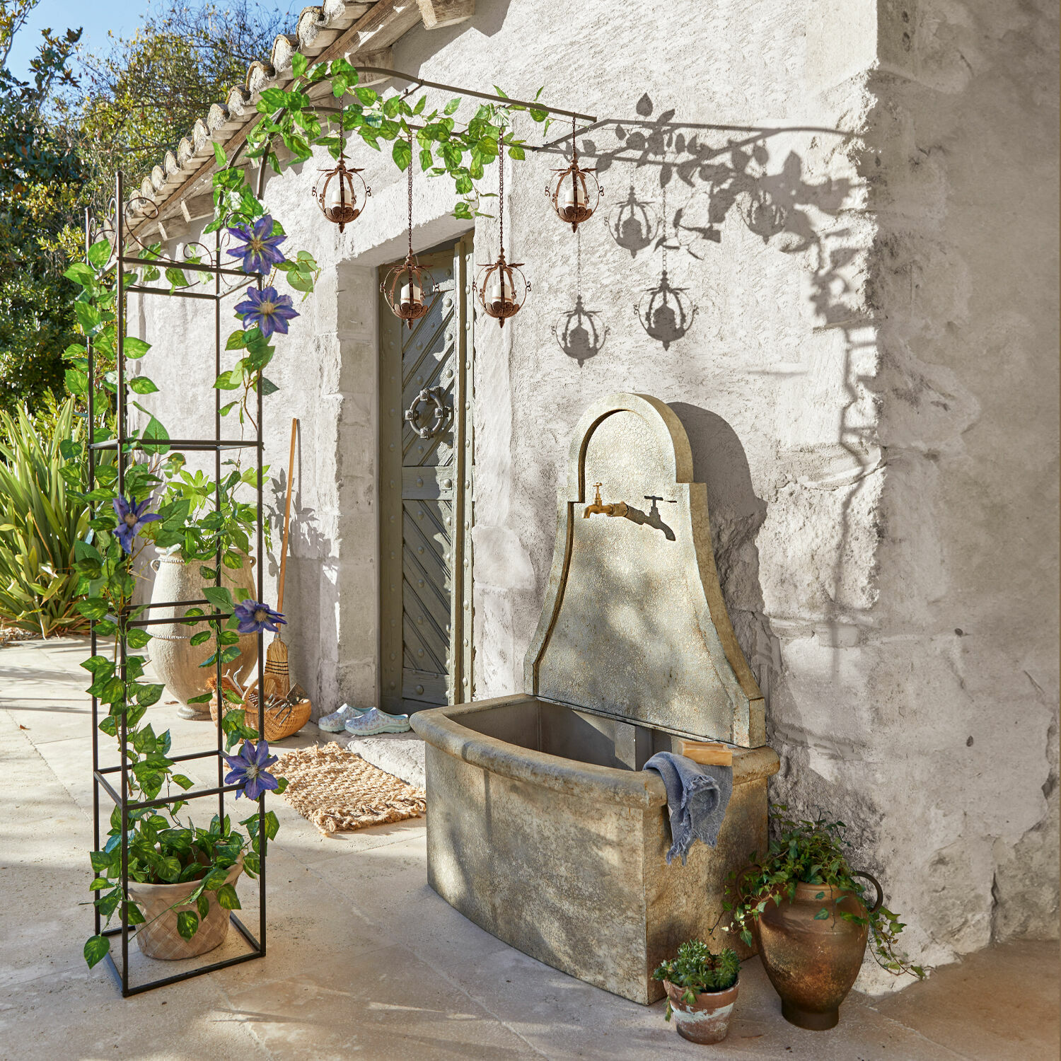 Garten mit steinernem Waschbecken und Metallpergola mit grünen Blättern und violetten Blüten