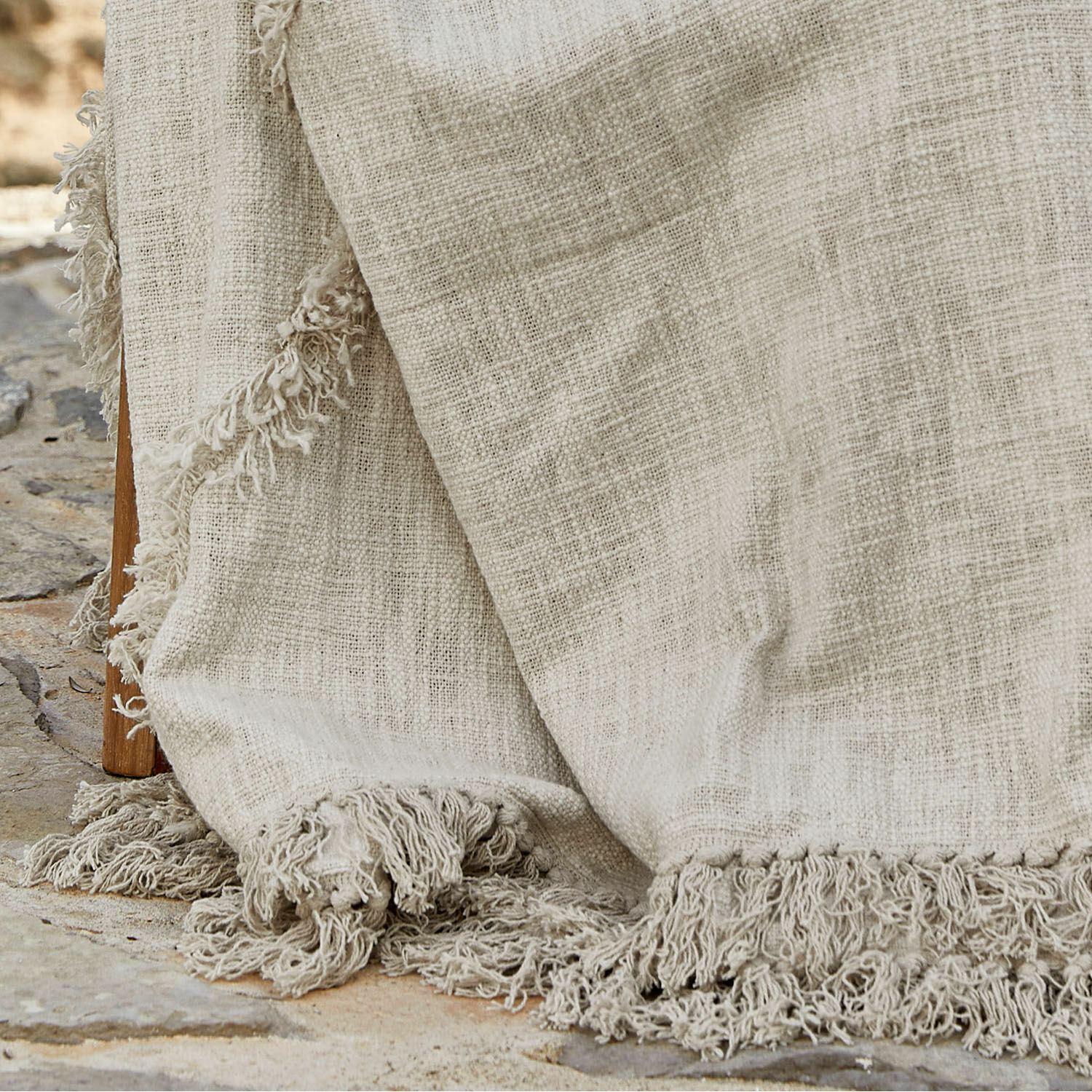 Beige Decke aus Naturstoff mit Fransen auf Steinboden, dekoratives Wohnaccessoire
