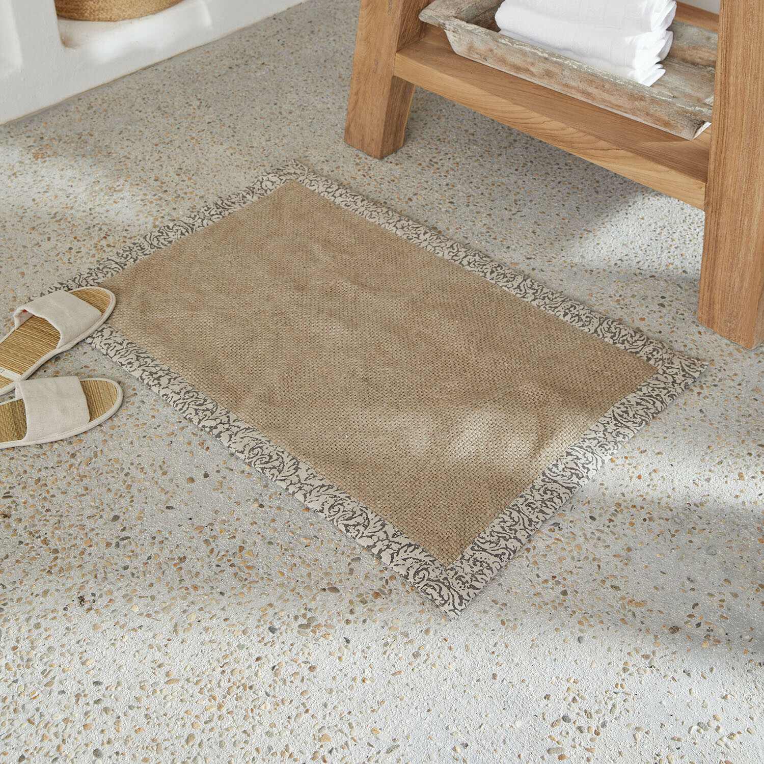 Beiger Teppich aus Naturmaterial mit dekorativem grauem Rand auf hellem Steinfussboden