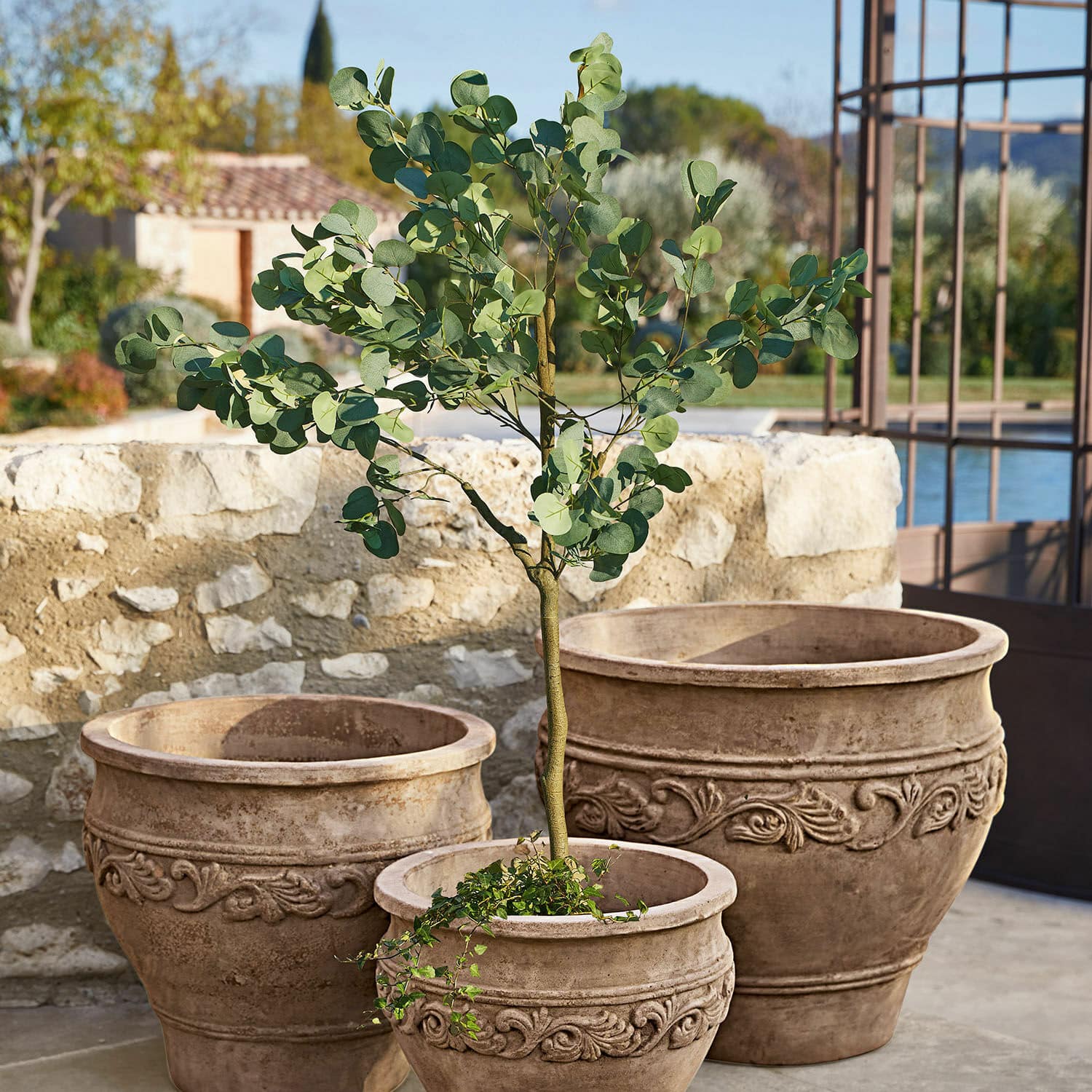 Drei dekorative Terrakotta-Pflanzgefäße in Naturfarbe mit Pflanze auf Terrasse