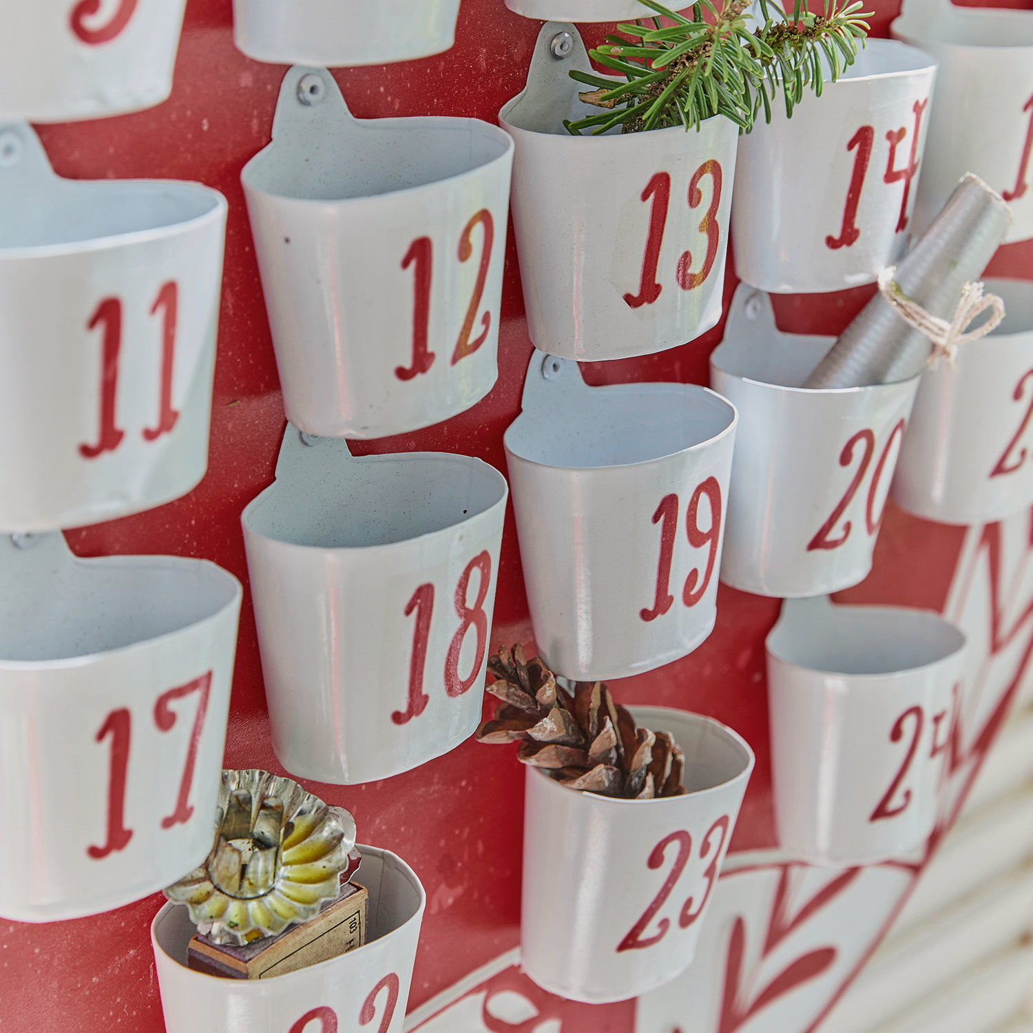 Adventskalender aus Metall mit weißen Behältern und roten Zahlen auf rotem Hintergrund