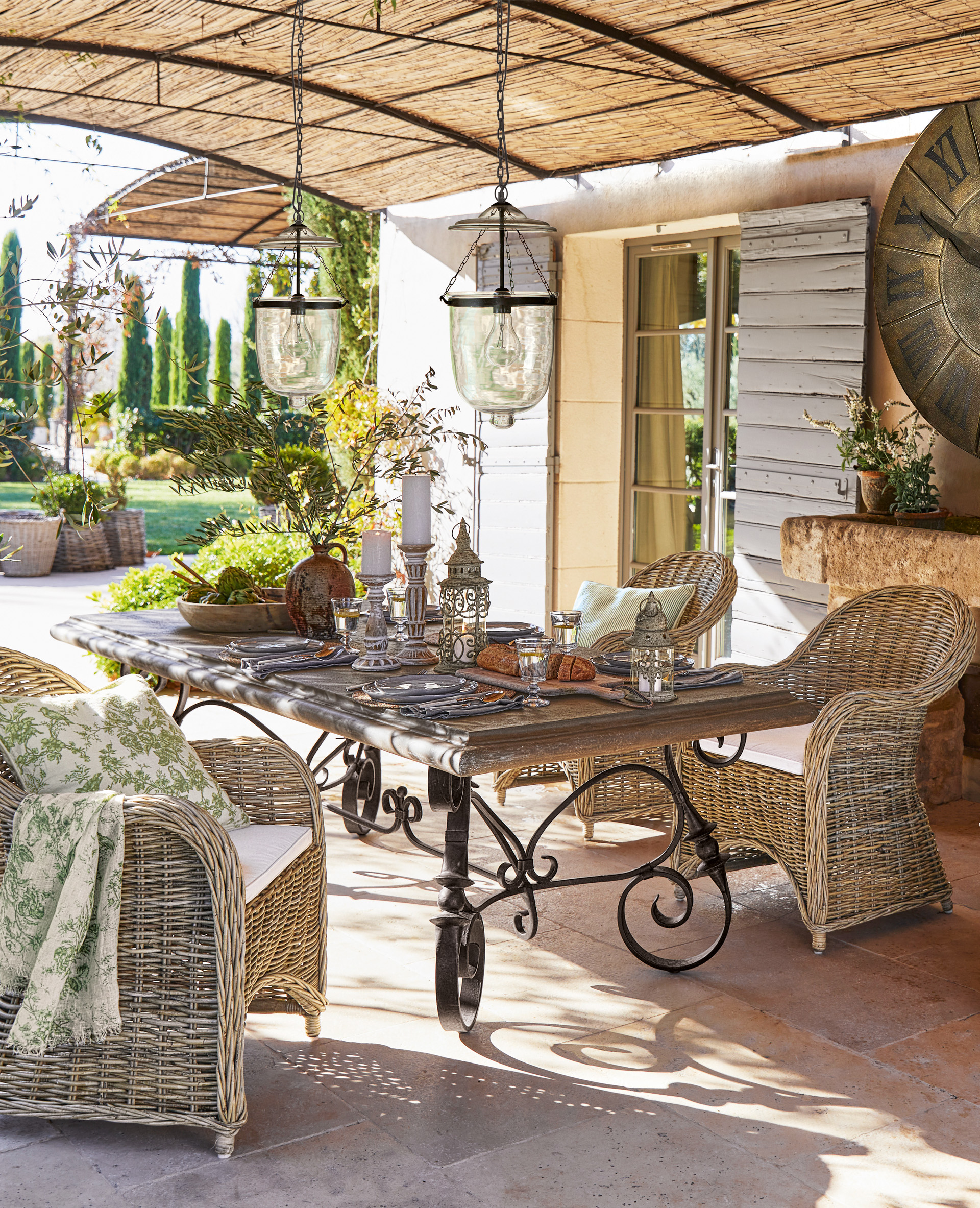 Rustikaler Gartentisch mit Eisenbeinen und Rattanstühlen auf Terrasse mit hängenden Lampen