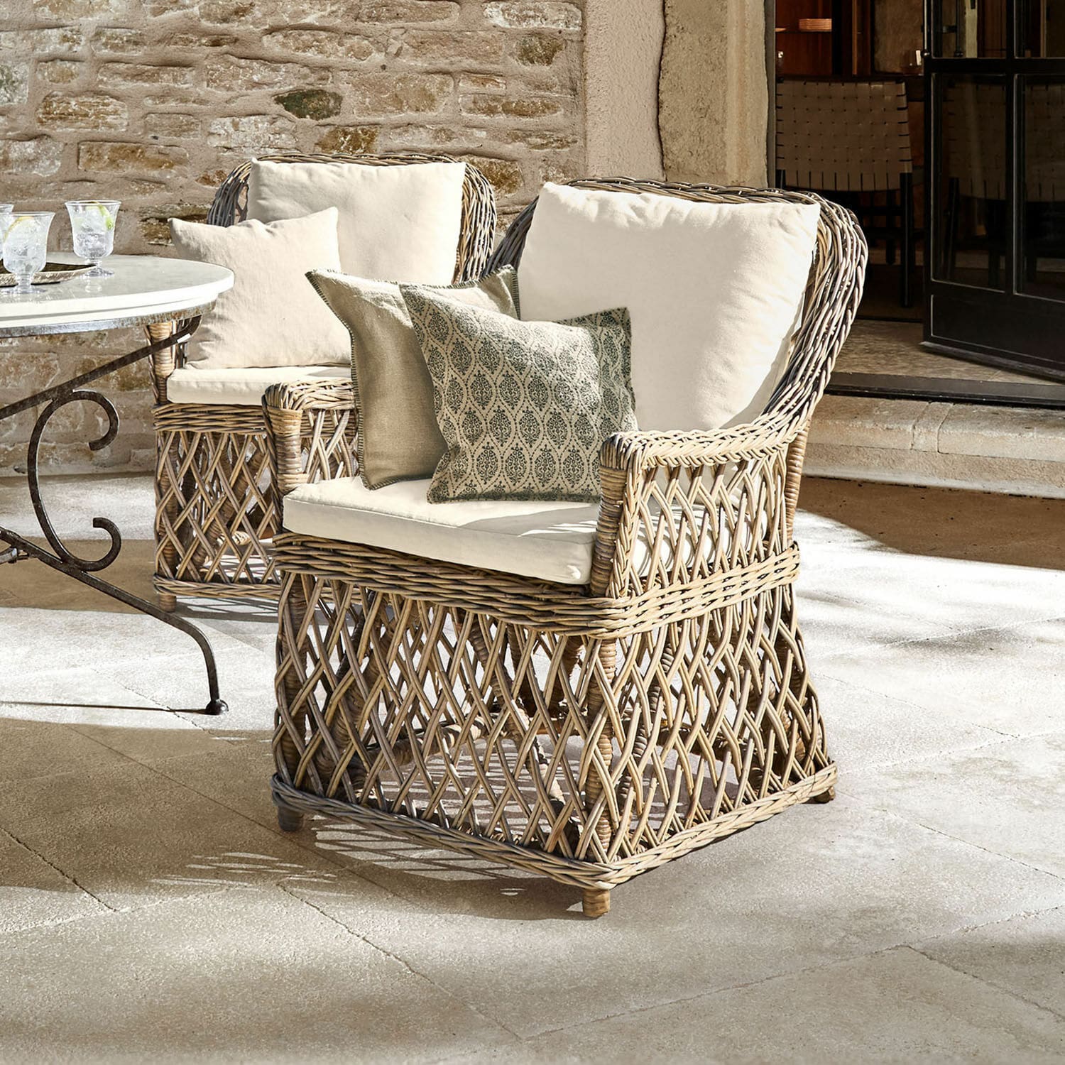 Sessel Nesvryn Bequemer Sessel aus natürlichem Rattan mit cremefarbenen Polstern und dekorativen Kissen für Terrasse.