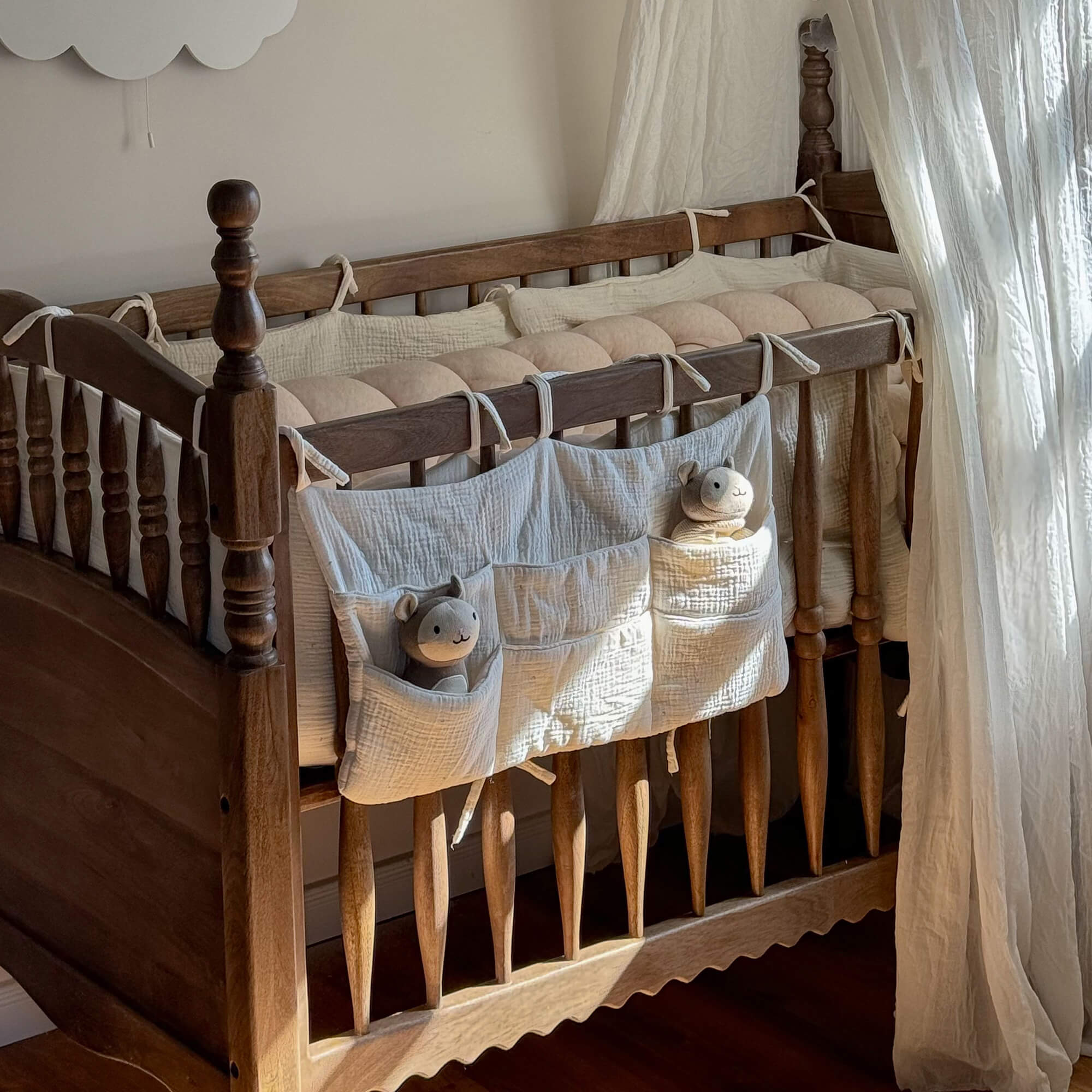 Kinderbett aus Holz mit cremefarbenem Baumwollschutz und Plüschtieren in den Taschen