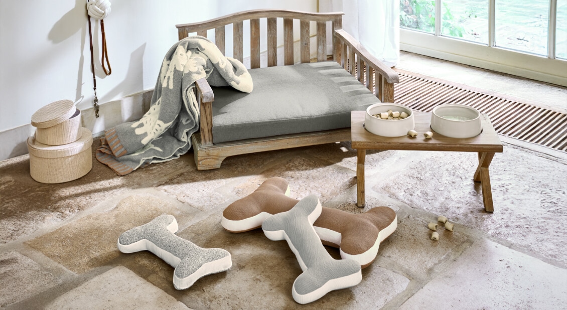 Holz-Hundebett mit grauem Kissen und Knochen-Spielzeugen auf Natursteinboden