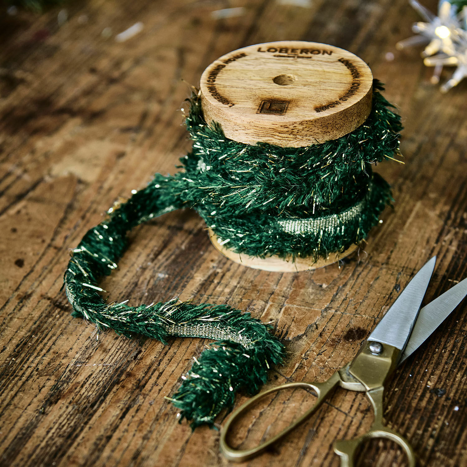 Band Calarith Grünes Dekoband mit metallischen Fäden auf Holzspule neben Schere auf Holztisch