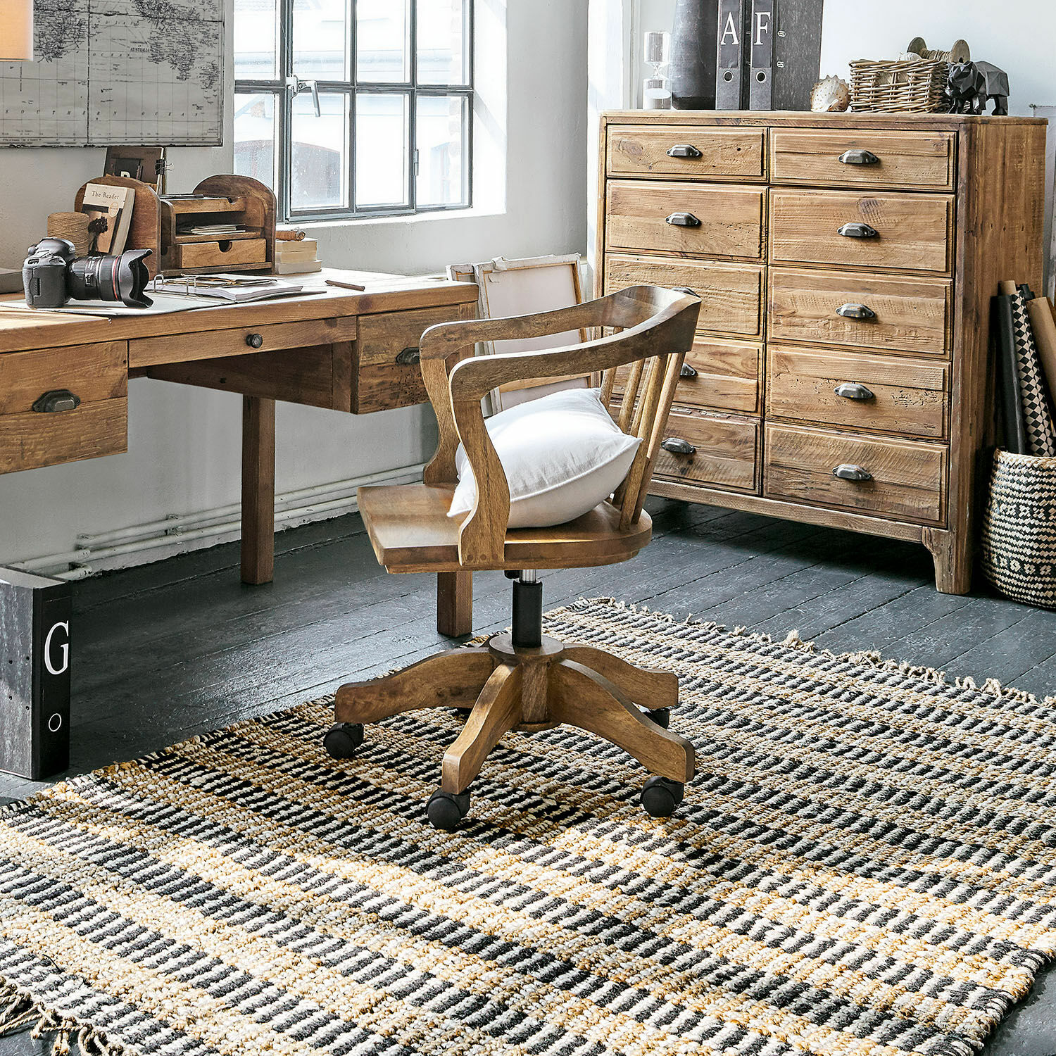 Holzschreibtisch und drehbarer Holzstuhl mit Kissen auf gewebtem Teppich in hellem Arbeitszimmer