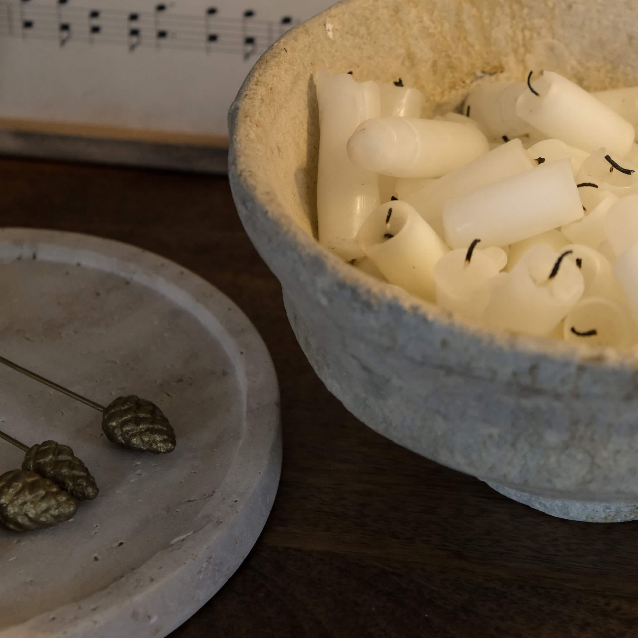 Schale aus Naturmaterial mit weißen Kerzen auf dunklem Holztisch, gemütliche Dekoration