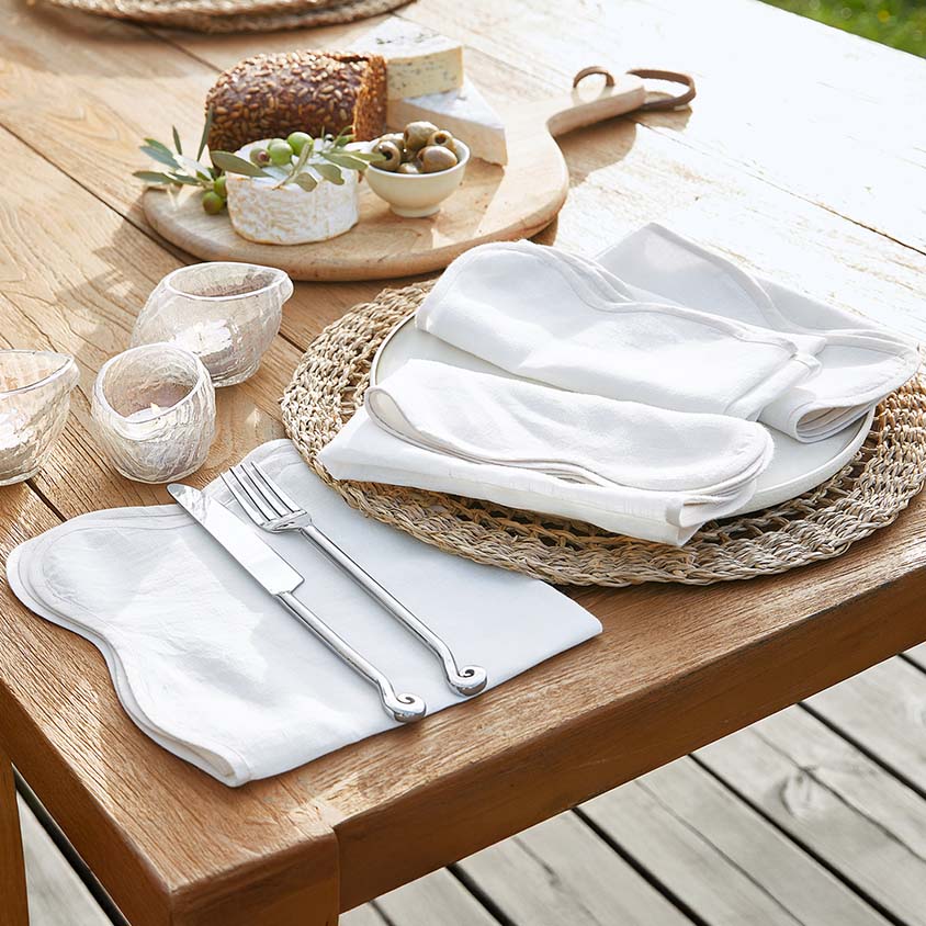 Weißes Leinen-Tischset mit Servietten und versilbertem Besteck auf Holztisch mit Snacks