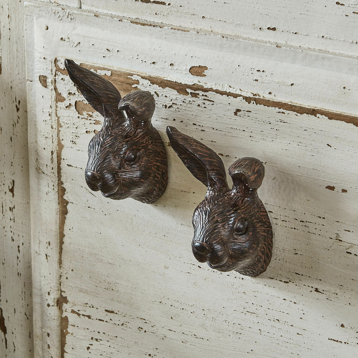 Zwei messingfarbene Möbelgriffe in Hasenkopf-Form an einem weiß gealterten Holzschrank