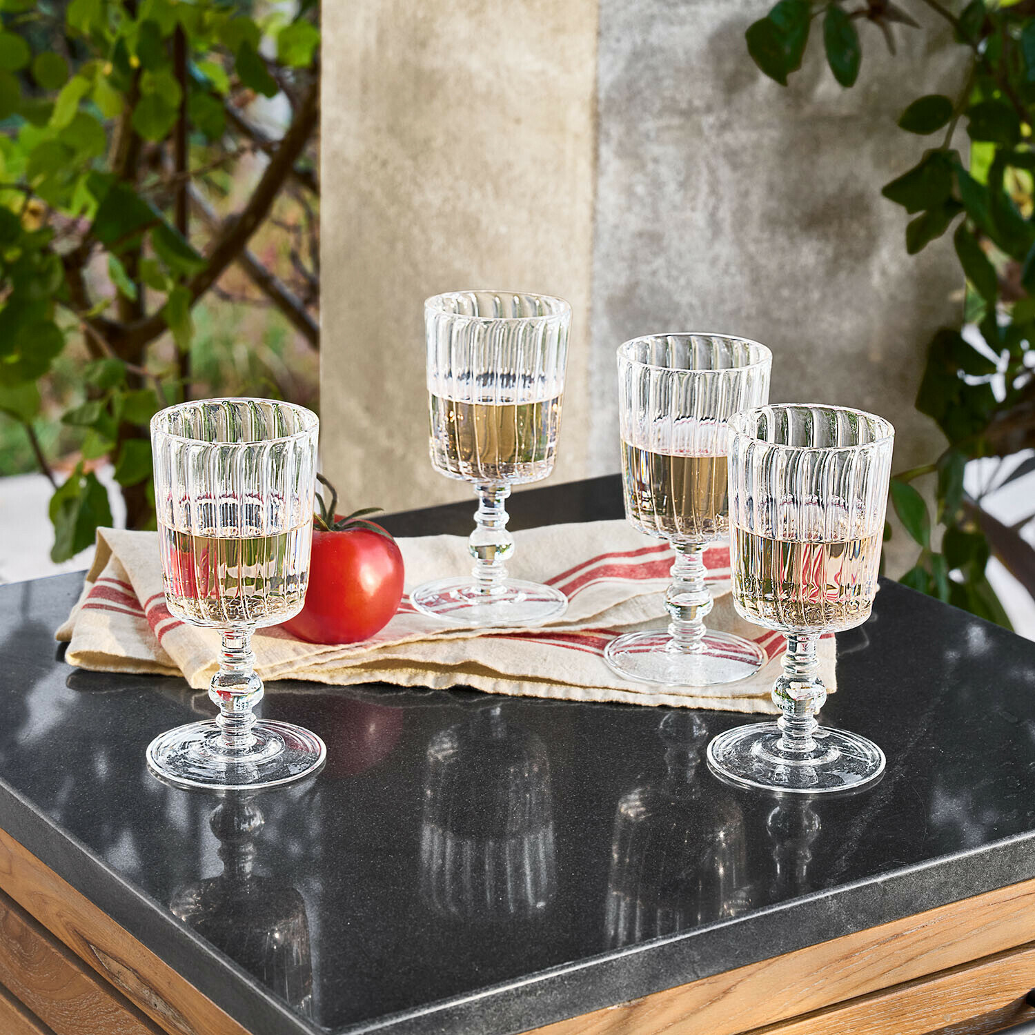 Glas 4er Set Lianzo Vier transparente, gerillte Gläser mit hellem Getränk auf schwarzer Tischplatte aus Stein