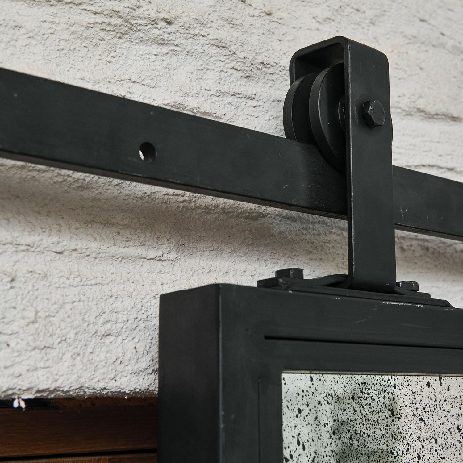 Schwarze Metallhalterung mit Rolle zur Wandbefestigung eines Spiegels an weißer Strukturwand