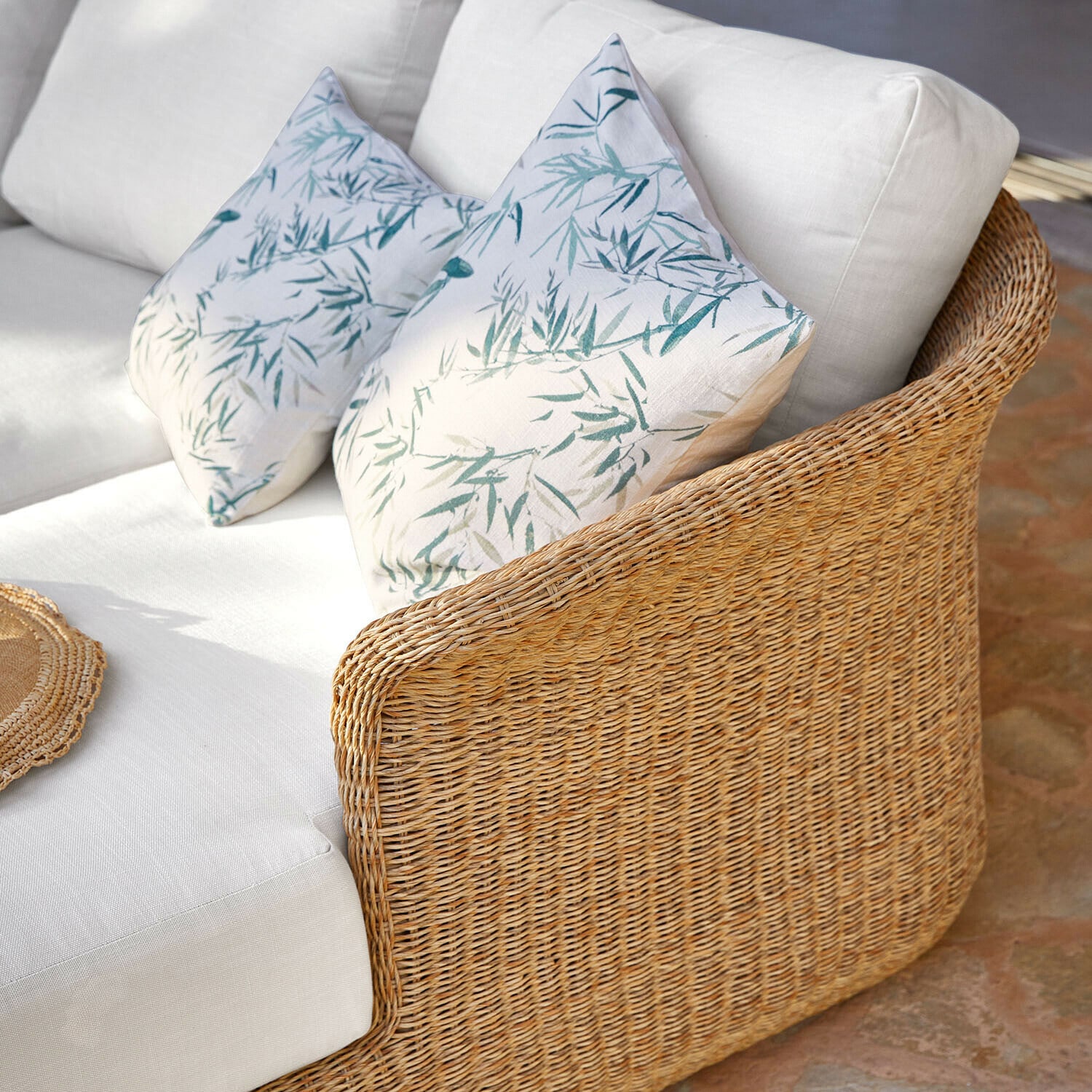 Rattansofa mit weißen Kissen und grünem Blattmuster, gemütliches Wohnzimmermöbel