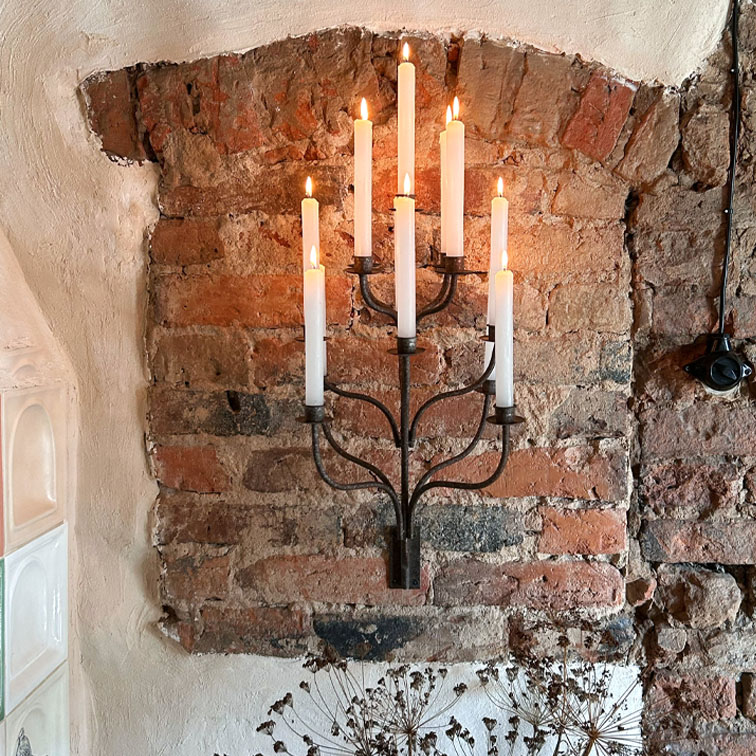 Metall-Wandkerzenhalter mit sieben weißen brennenden Kerzen vor einer Ziegelsteinwand, Wohnaccessoire