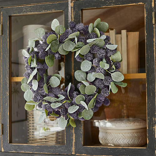 Dekorativer Kranz mit grünen Blättern und violetten Blüten an schwarzem Holzschrank