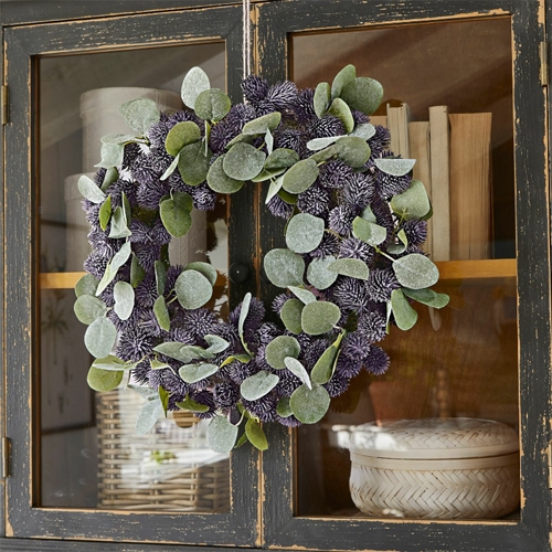 Dekorativer Kranz mit grünen Blättern und violetten Blüten an schwarzem Holzschrank