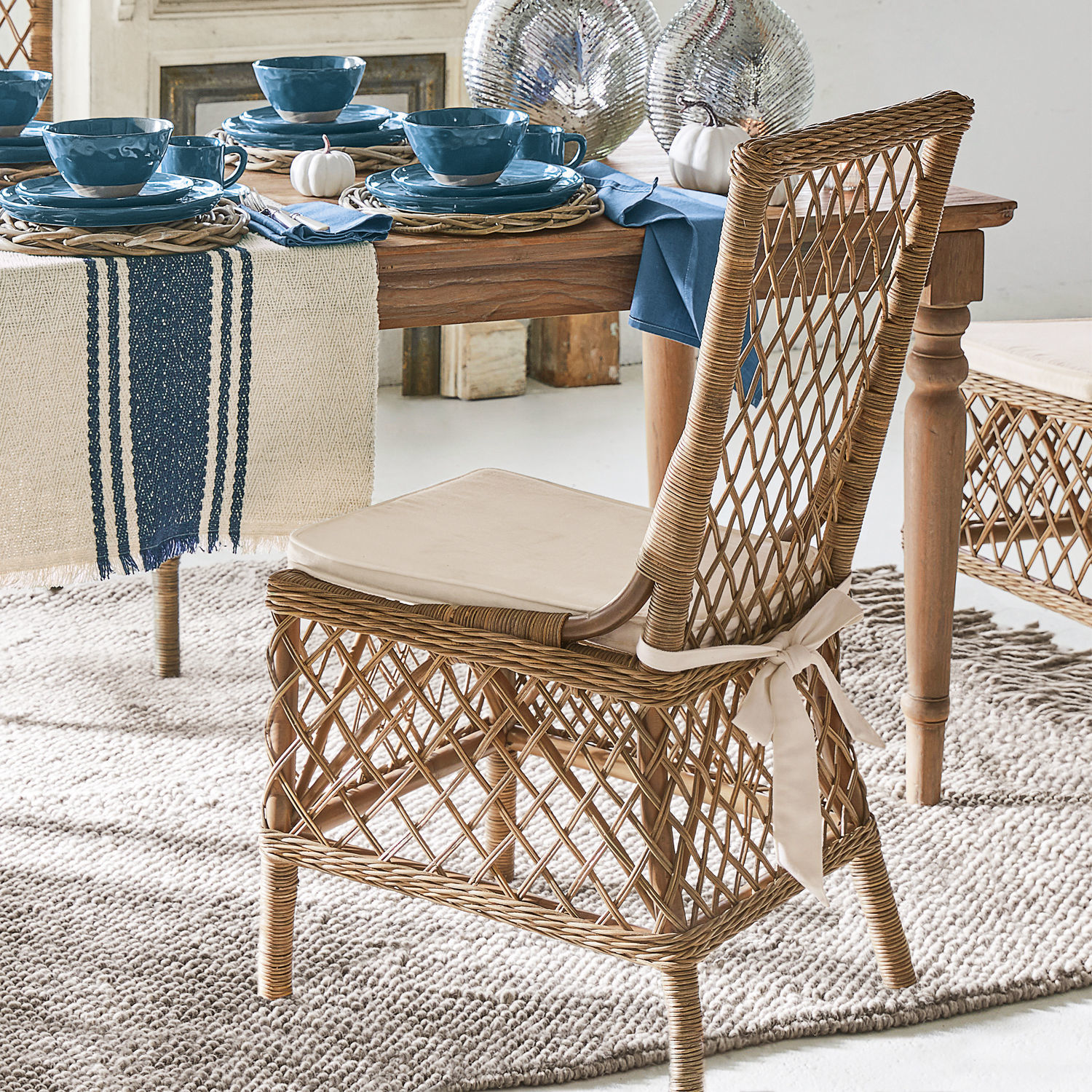 Rattanstuhl mit cremefarbenem Kissen und geflochtenem Rückenlehne am Holztisch mit blauer Geschirrserie
