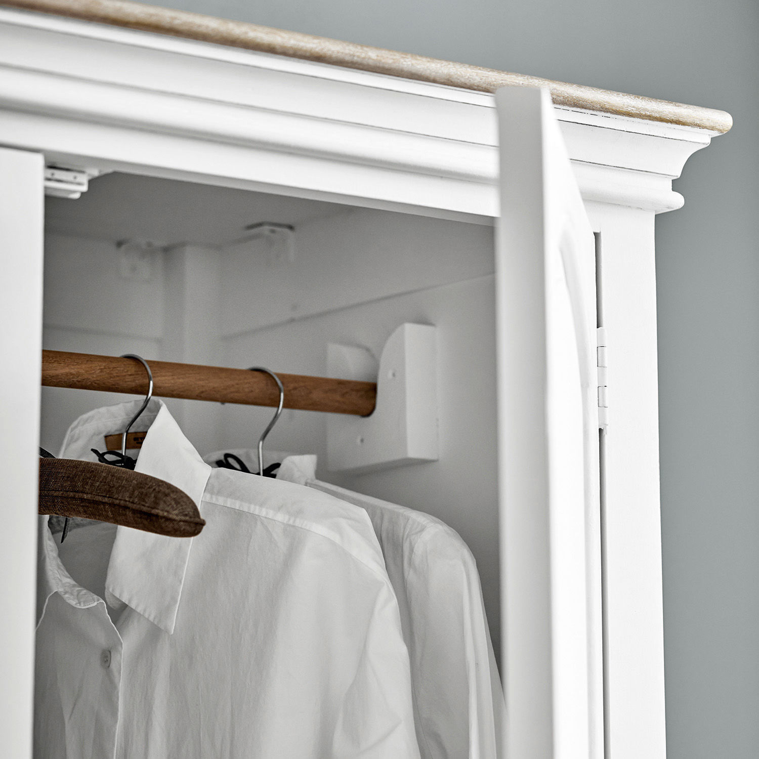 Weißer Holzkleiderschrank mit Holzstange und weißen Hemden an Metallbügeln