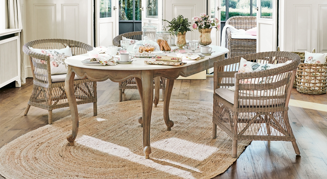 Esszimmer mit rustikalem Holztisch und Korbstühlen auf rundem Jute-Teppich im Landhausstil
