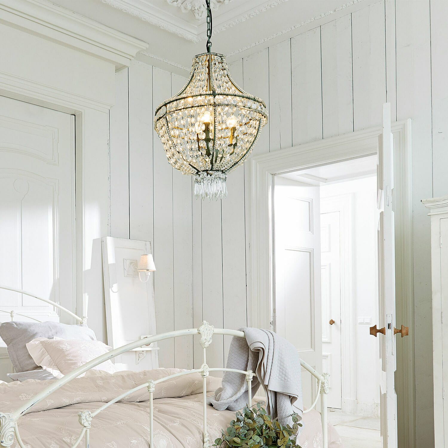 Kristall-Kronleuchter aus Metall und Glas in weißem Schlafzimmer mit Bett und heller Bettwäsche