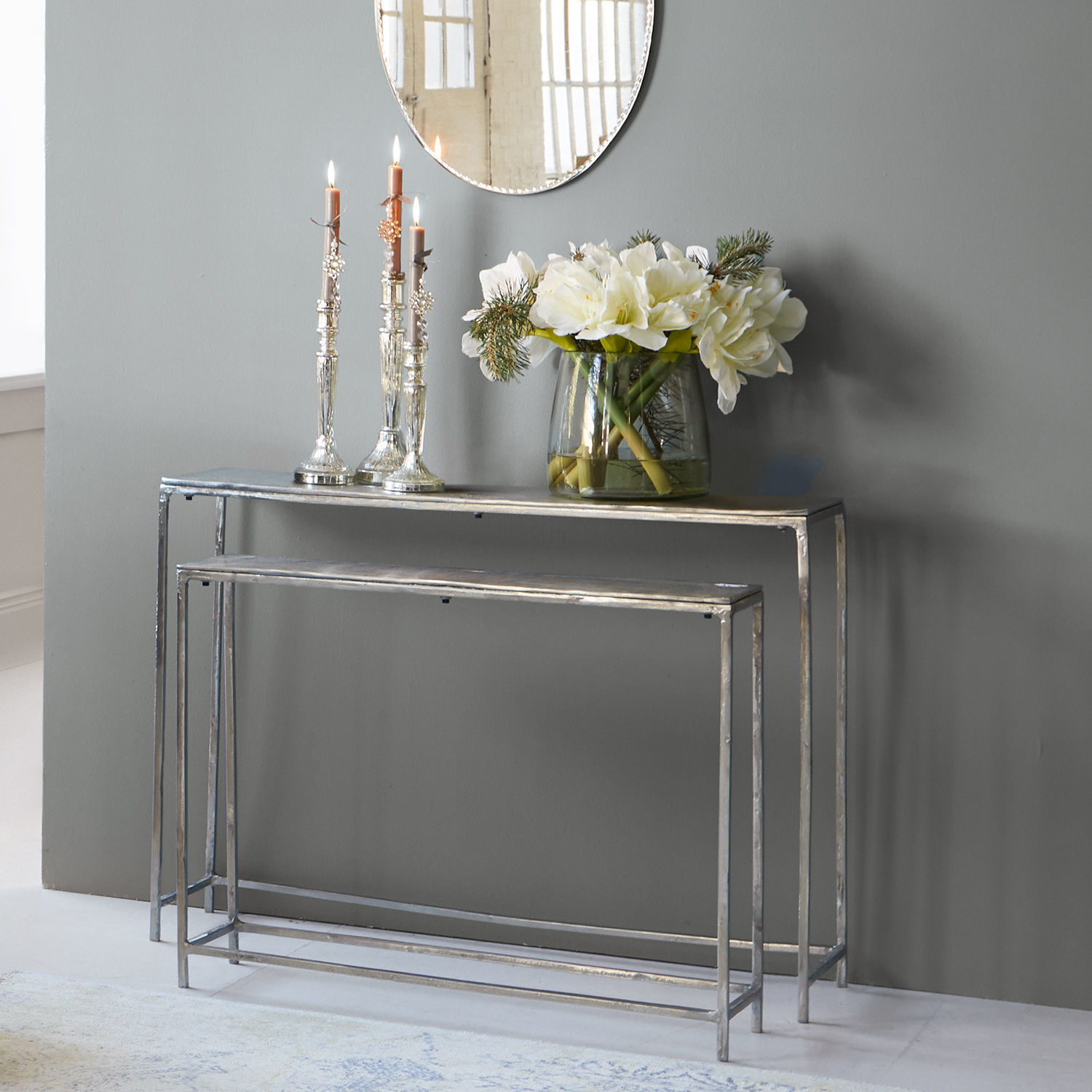 Set aus zwei silbernen Metallkonsolen mit dekorativen Kerzen und weißen Blumenarrangements