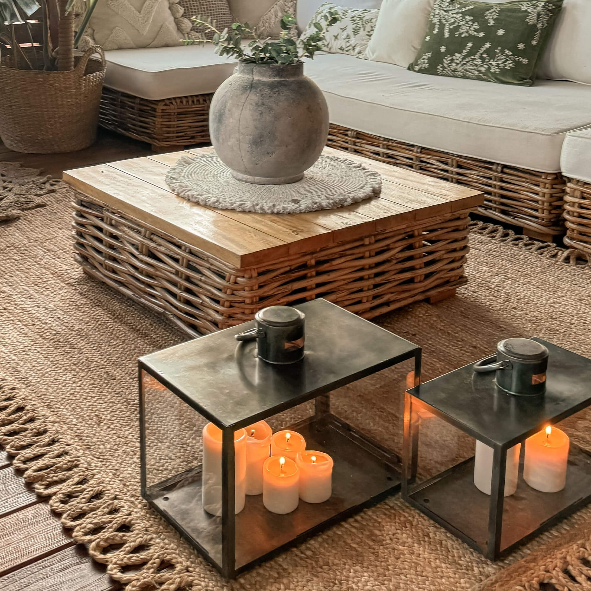 Metall-Laternen mit weißen Kerzen auf Juteteppich in gemütlichem Wohnzimmer mit Rattantisch