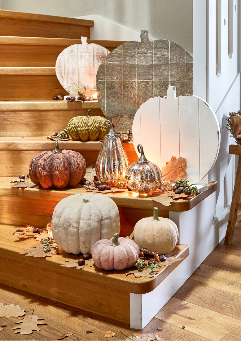 Herbstliche Dekoration mit Holz- und Stoffkürbissen in Pastellfarben auf Holztreppe mit Laub