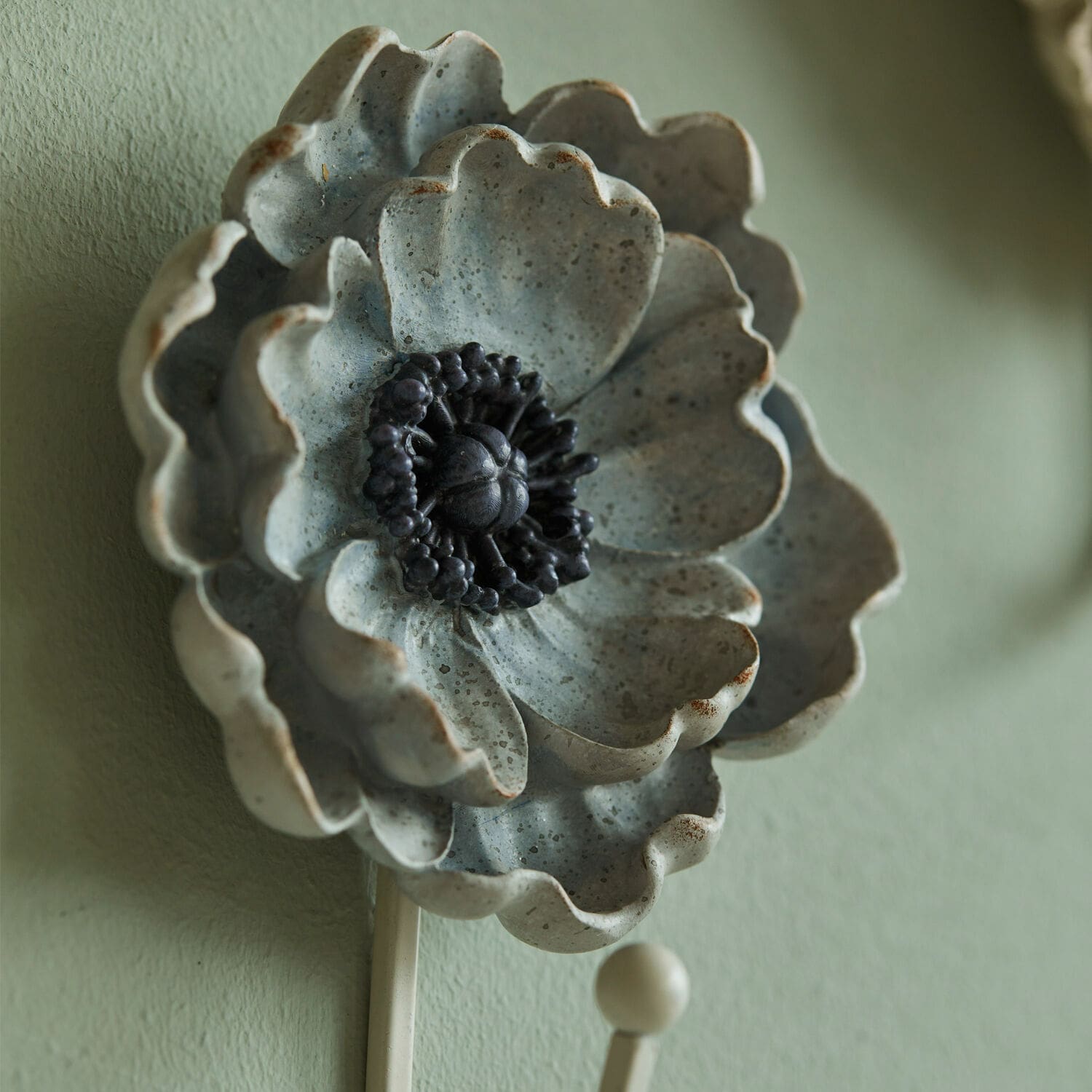 Dekorativer Wandhaken in Form einer grauen Keramikblume mit schwarzem Zentrum