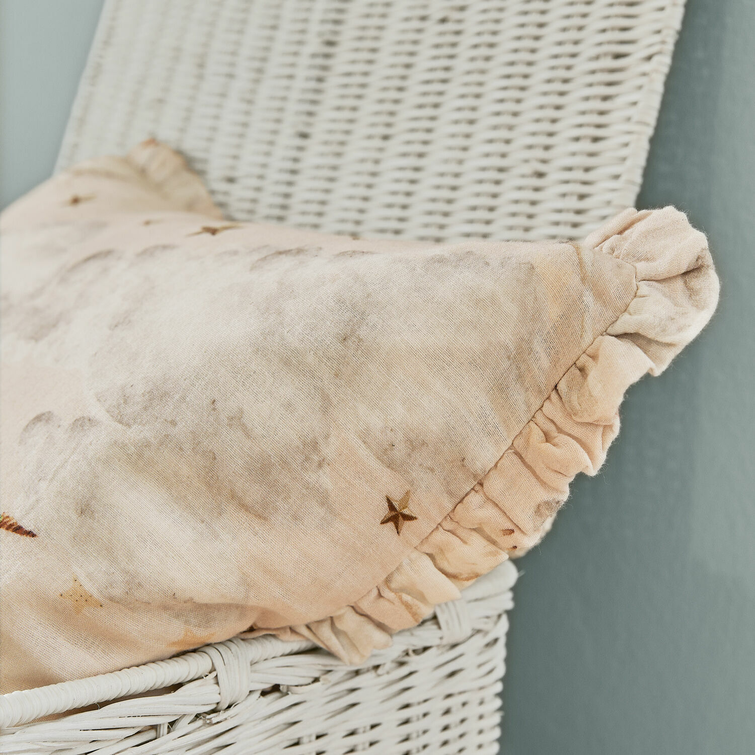 Beige Leinenkissen mit Rüsche und Sternmotiv auf weißem Korbsessel