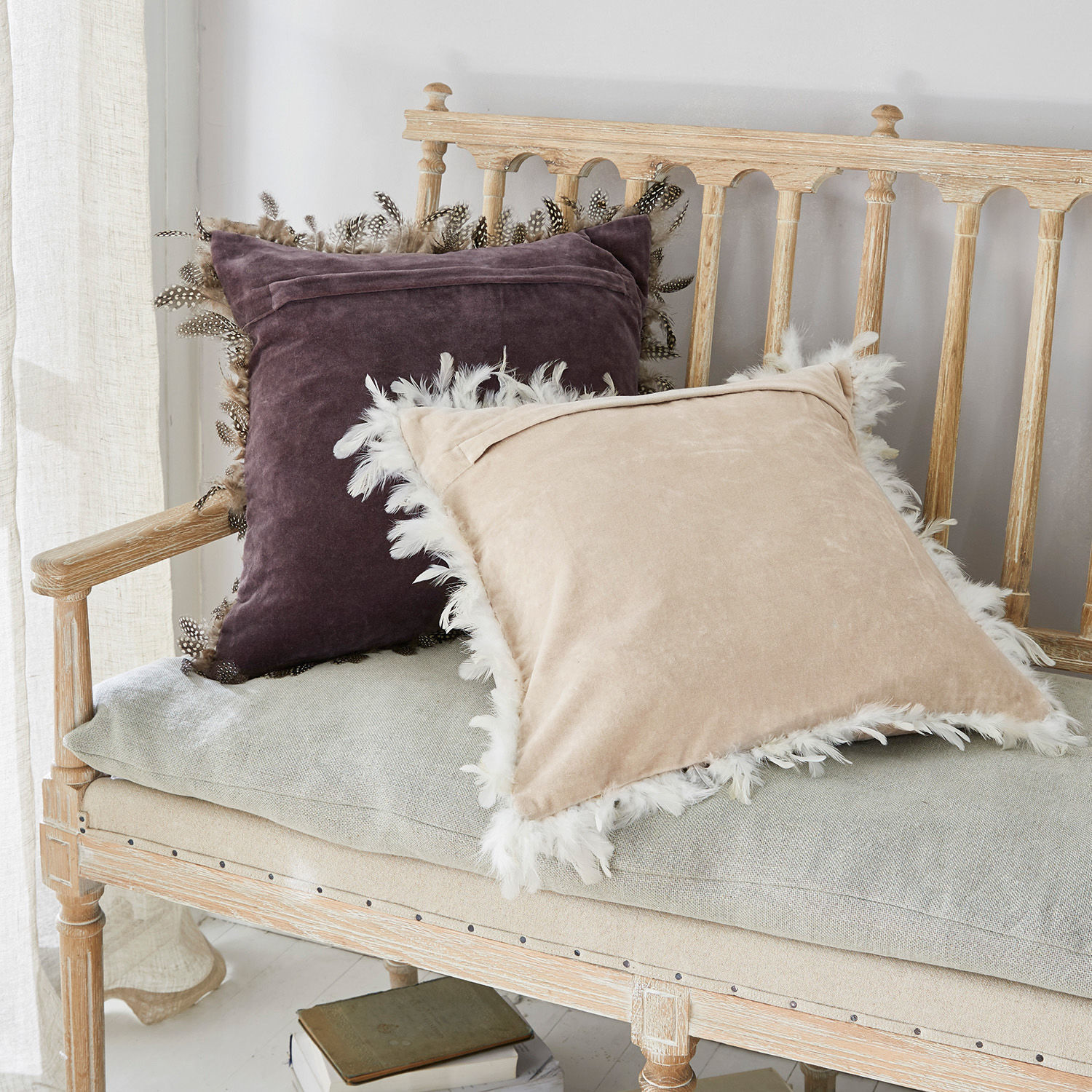 Zwei dekorative Samtkissen mit Federn in Beige und Violett auf einer hellen Holzbank