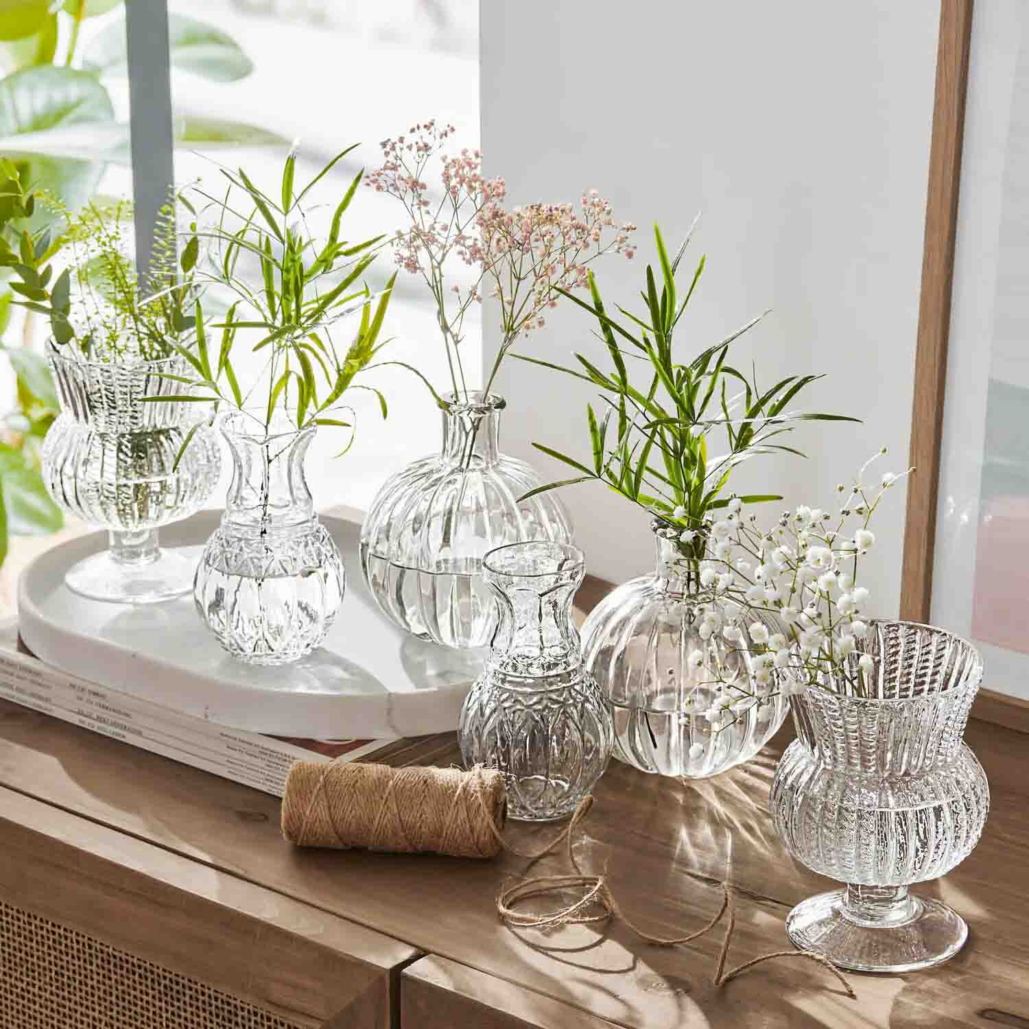 Set aus transparenten Glasvasen mit grünen und weißen Blumen auf einem Holzsideboard