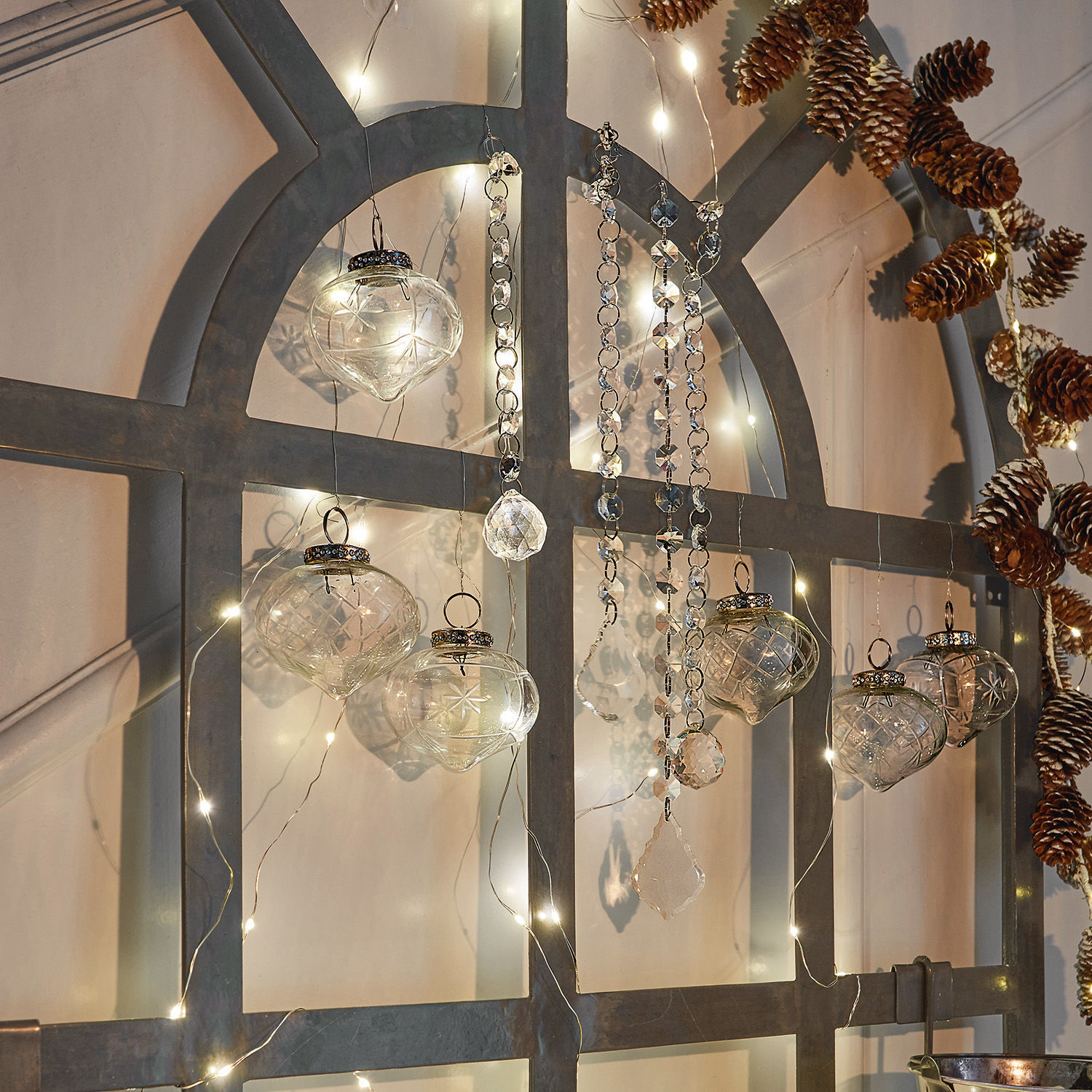 Glasornamente mit Kristallanhängern und LED-Lichterkette an grauem Metallrahmen