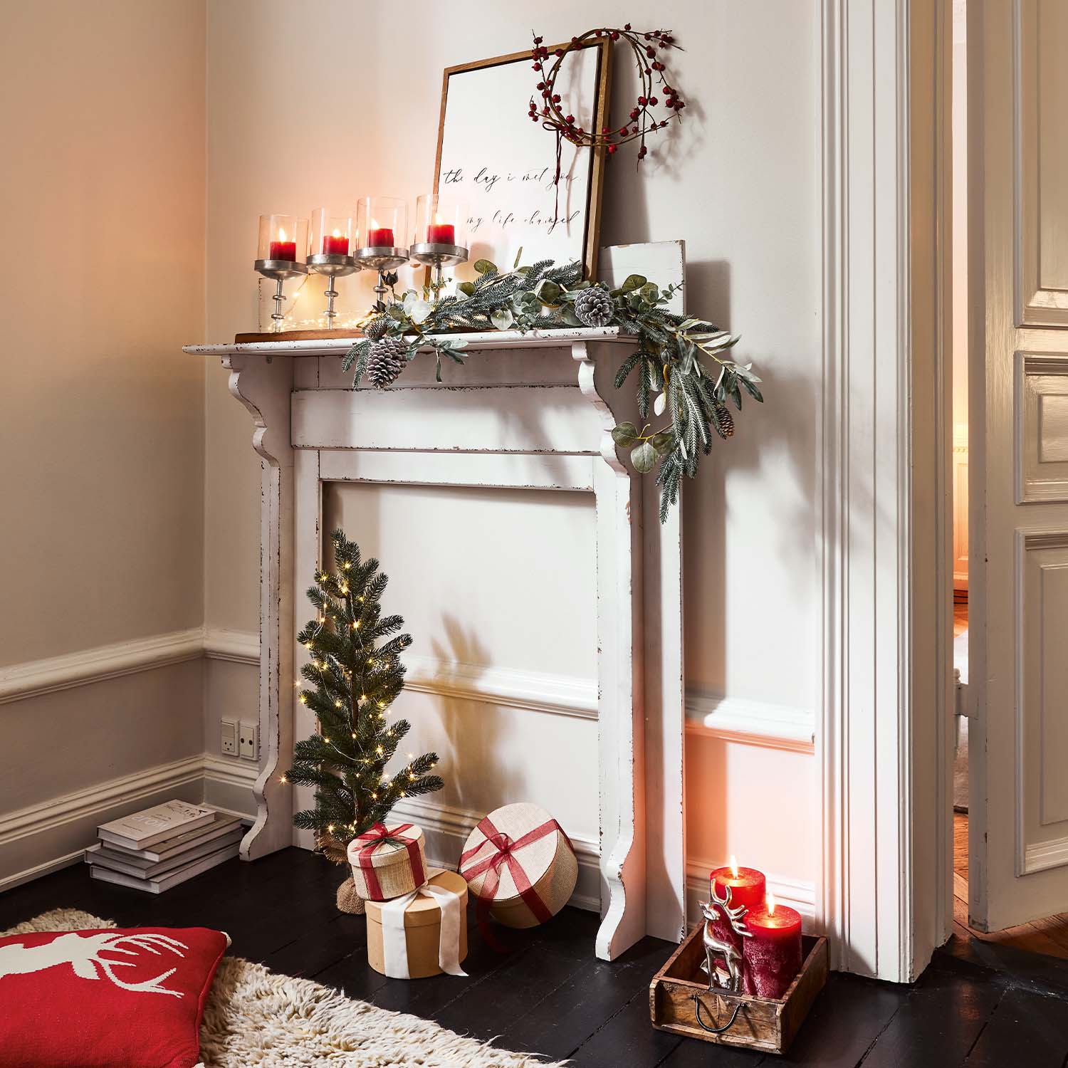 Weißer Holz-Kamin mit Weihnachtsdekoration, roten Kerzen und verpackten Geschenken auf dem Boden