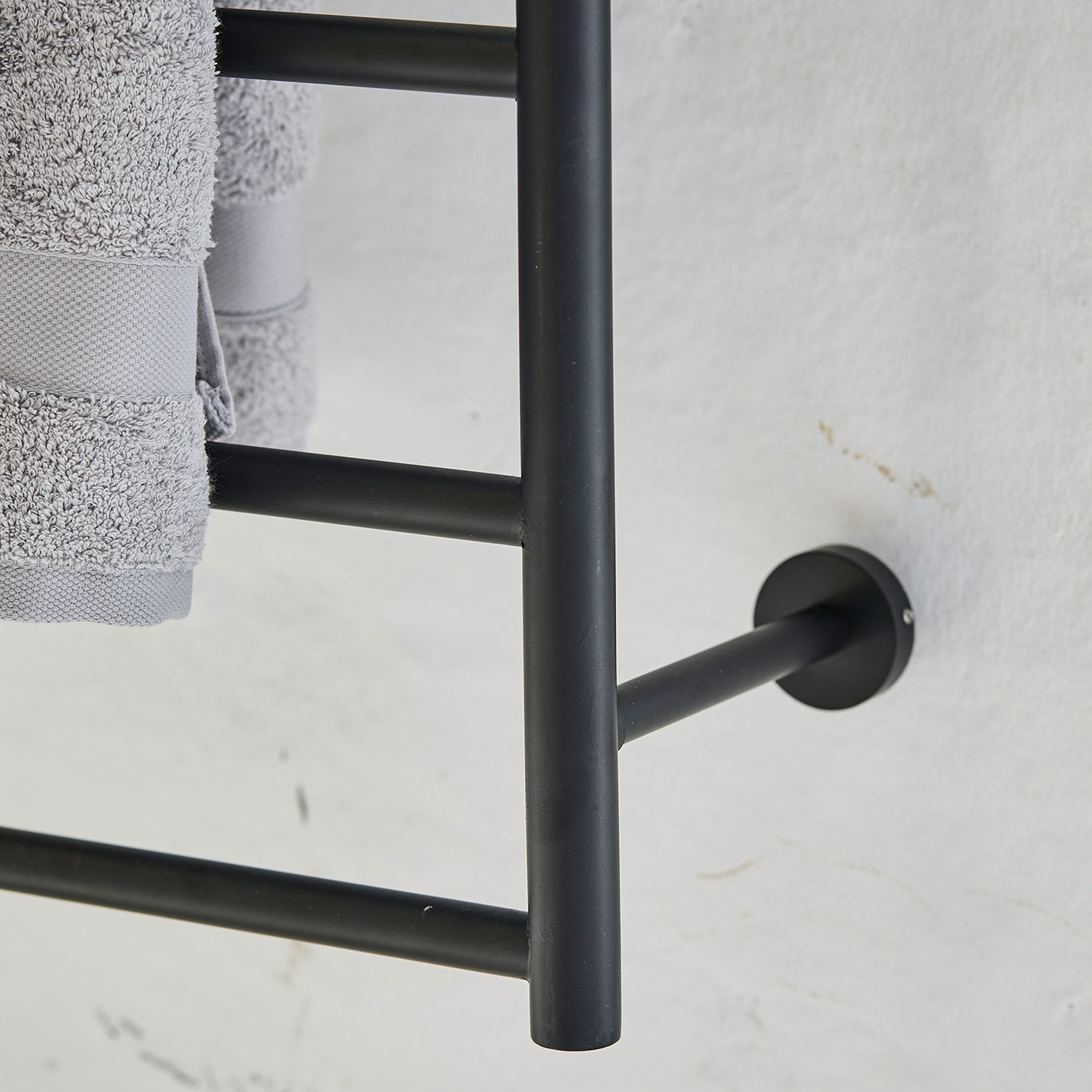 Schwarzer Metall-Handtuchhalter mit grauen Handtüchern an weißer Wand im Badezimmer