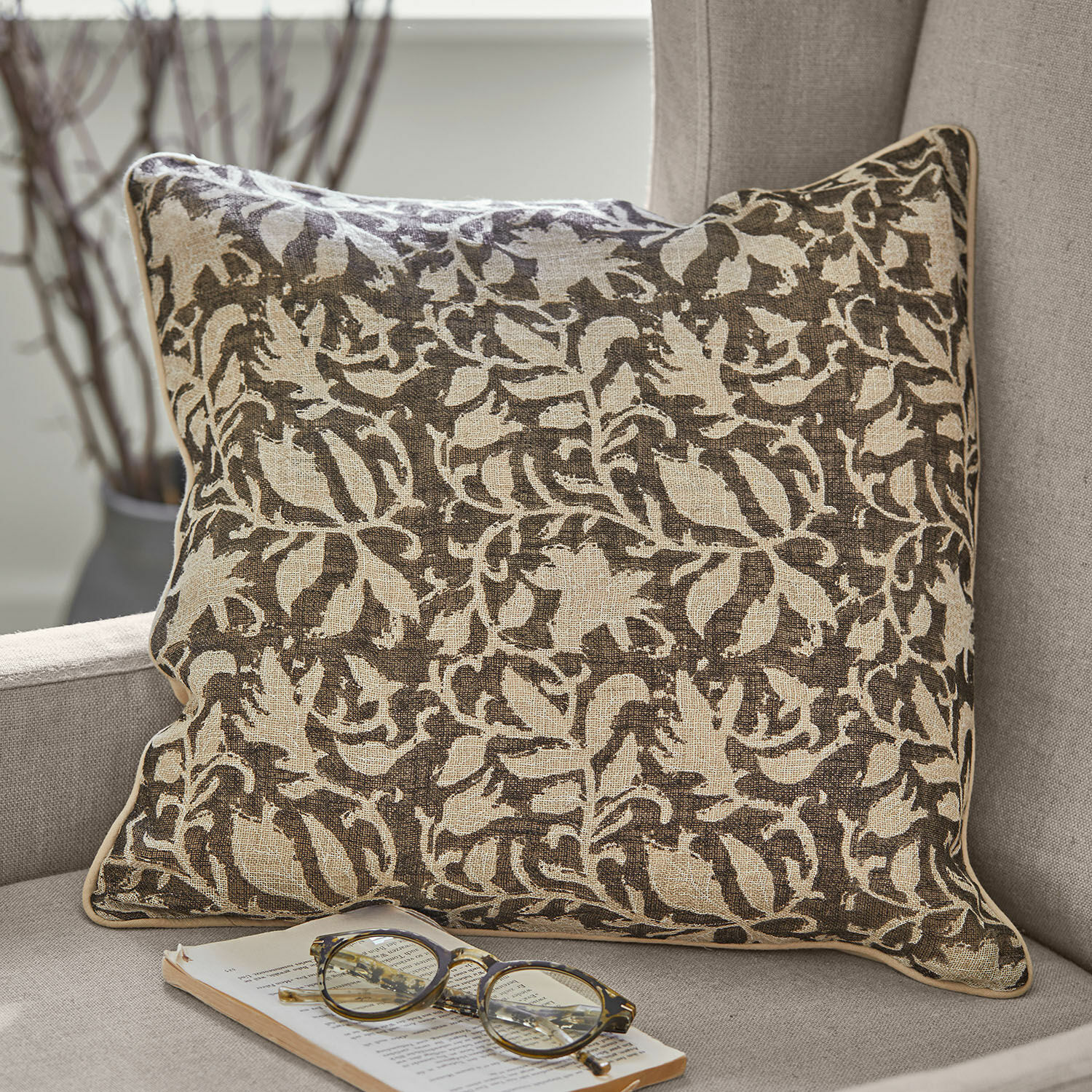 Kissenhülle 2er Set Ziradayn Braun-beiges Baumwollkissen mit floralem Muster auf grauem Sofa mit Brille und Buch