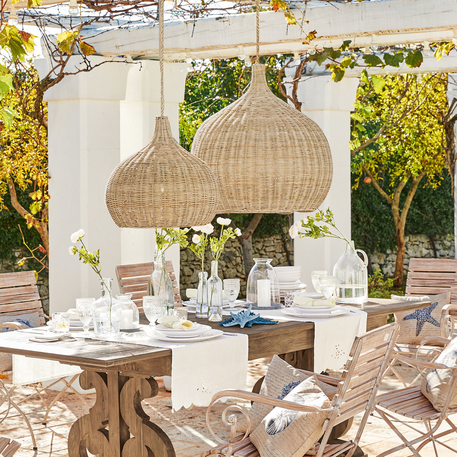 Gartenmöbel-Set mit Holztisch und naturfarbenen Rattan-Hängeleuchten im Außenbereich