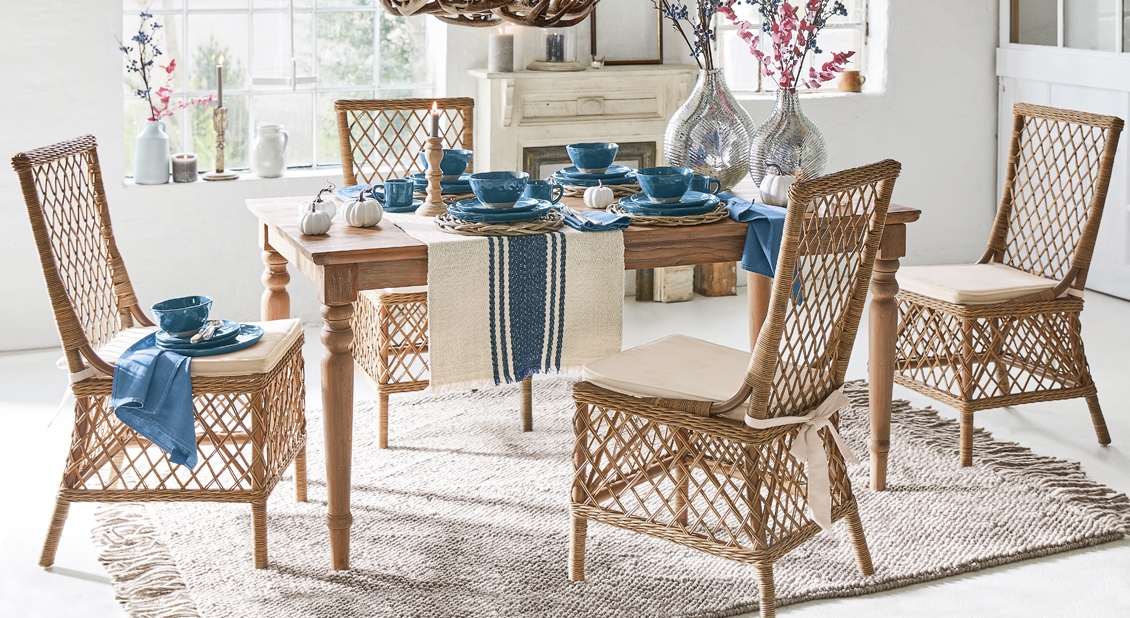Esszimmer mit Holztisch und Rattanstühlen mit beigen Kissen und blauem Geschirr