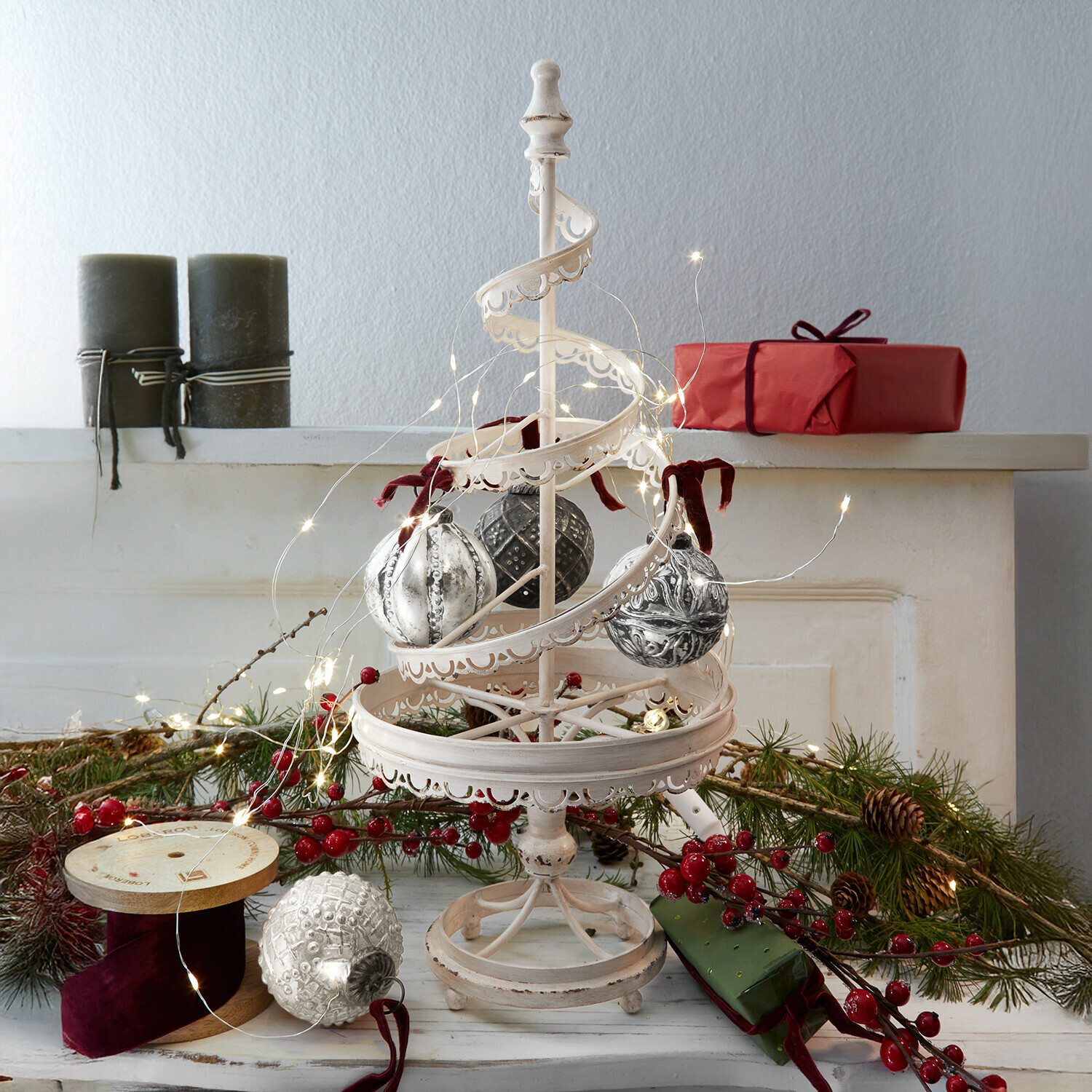 Deko-Baum Gerzat Weisse Metall-Weihnachtsdekoration mit hängenden Kugeln und LED-Lichterkette, rote Geschenke und Tannenzweige im Hintergrund