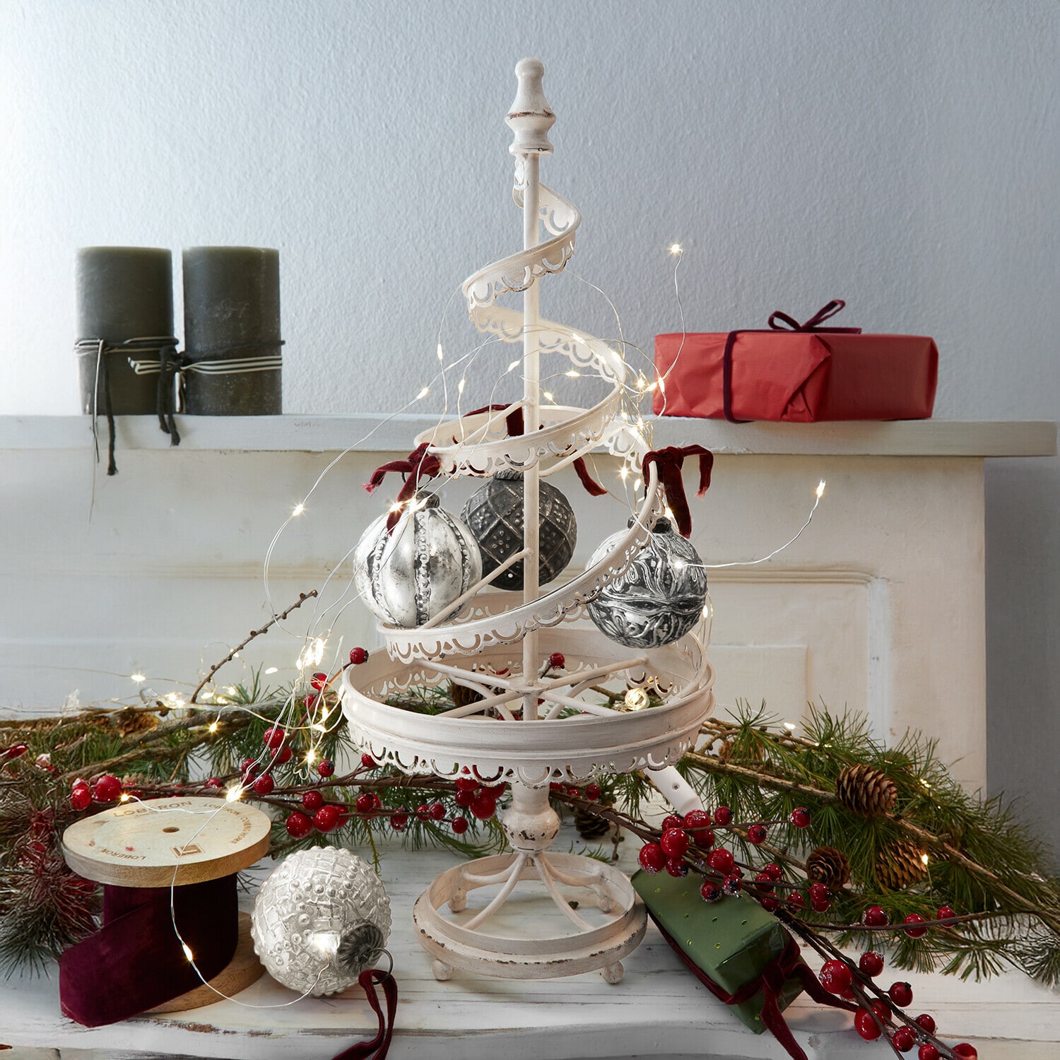 Deko-Baum Gerzat Weisse Metall-Weihnachtsdekoration mit hängenden Kugeln und LED-Lichterkette, rote Geschenke und Tannenzweige im Hintergrund