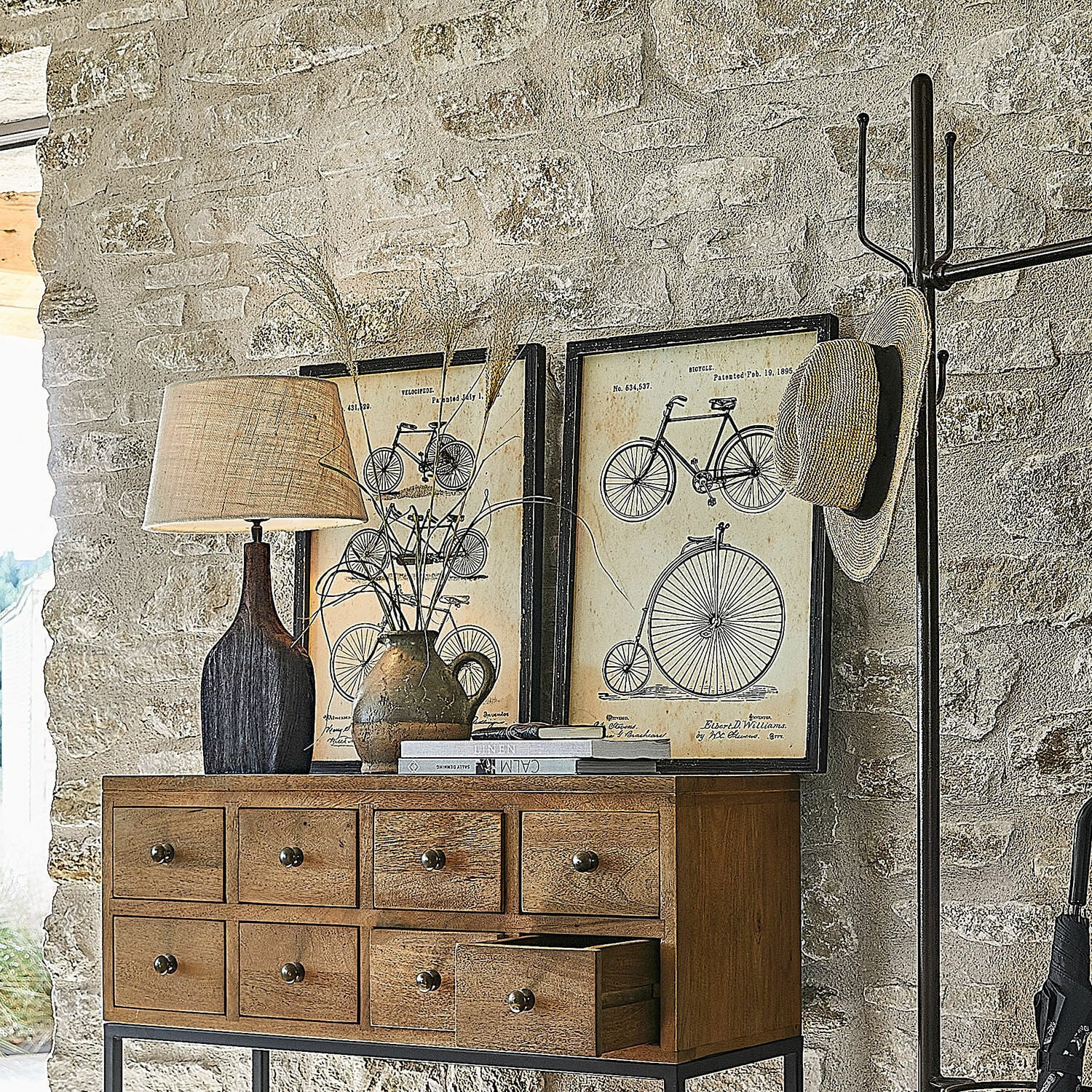 Holzkommode mit neun Schubladen, Lampe und Dekorationen vor rustikaler Steinwand im Landhausstil