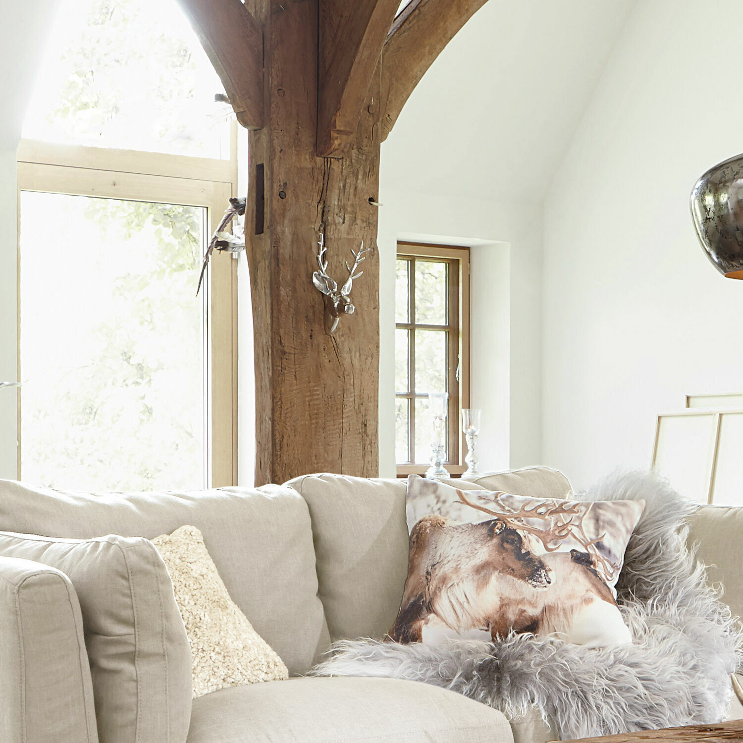 Beiges Sofa mit Rentier-Kissen und grauem Fellüberwurf in hellem Wohnzimmer mit Holzträger