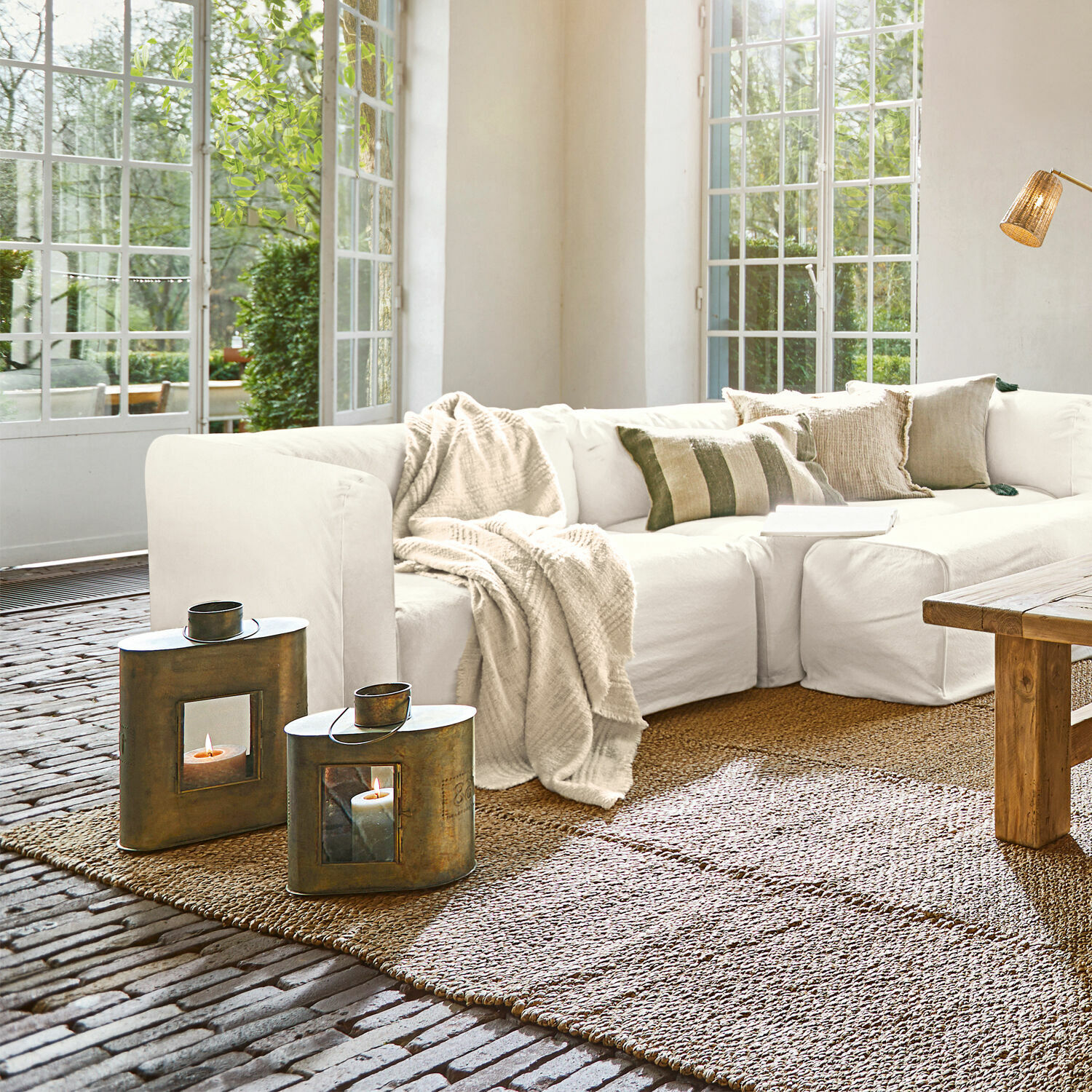 Gemütliches Wohnzimmer mit weißem Sofa, Leinen-Decke und kupfernen Laternen auf natürlichem Jute-Teppich